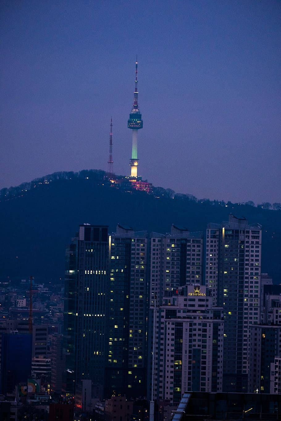korean 桌布 壁紙 — 黃昏城市景觀，亮燈的N首爾塔矗立在山丘上，俯瞰著發光的高層建築。