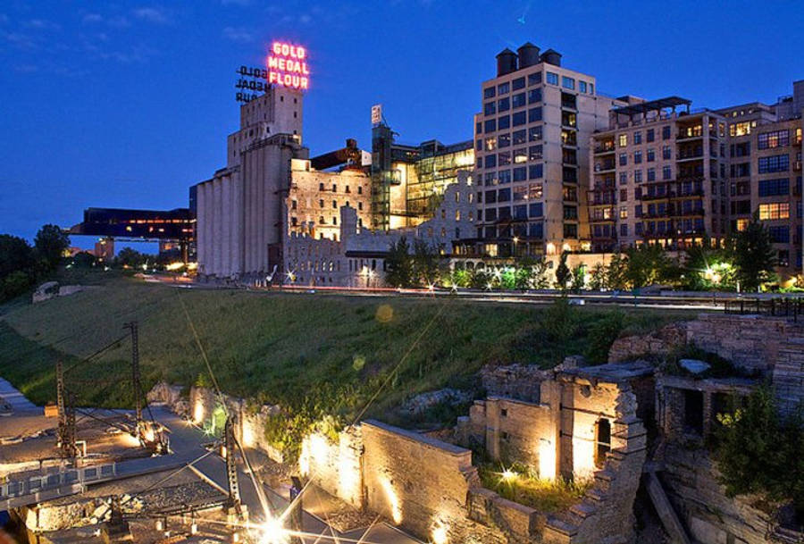 Minneapolis 桌布 壁紙 — 黃昏城市景觀，特色是歷史悠久的穀倉，旁邊有發光的霓虹燈標誌，現代公寓建築和下方被照亮的廢墟。