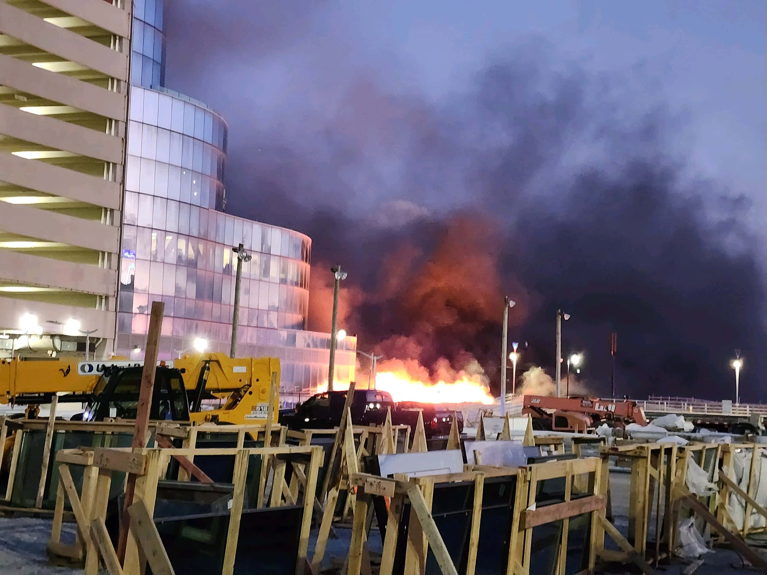 火焰動畫 桌布 壁紙 — 黃昏天空下，一座現代玻璃建築附近的建築工地發生猛烈火災。