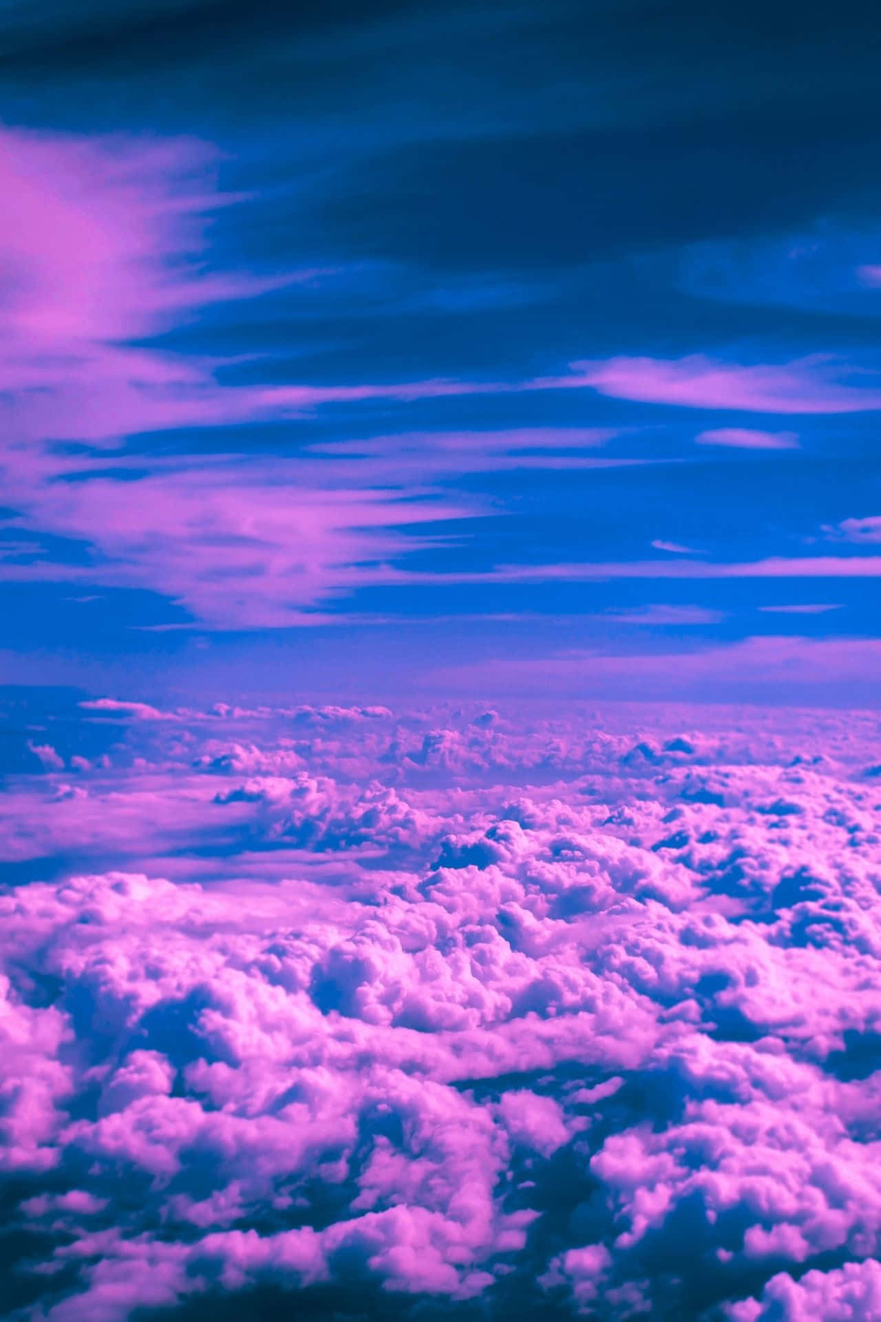 Trippy Aesthetic Cloud 桌布 壁紙 — 黃昏天空下，蓬鬆雲朵在鮮豔粉紅與深藍色調中閃耀的航拍視角。