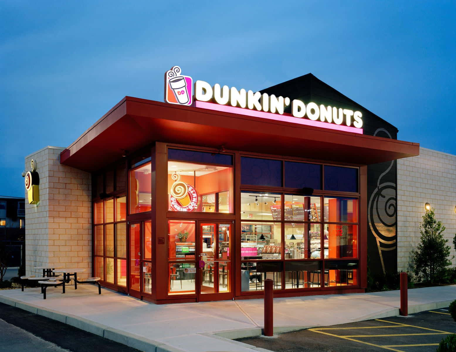 Dunkin Donuts 桌布 壁紙 — 黃昏時分，Dunkin' Donuts 店鋪正面燈火通明，內部溫暖光線與紅色外部裝飾相映成趣。