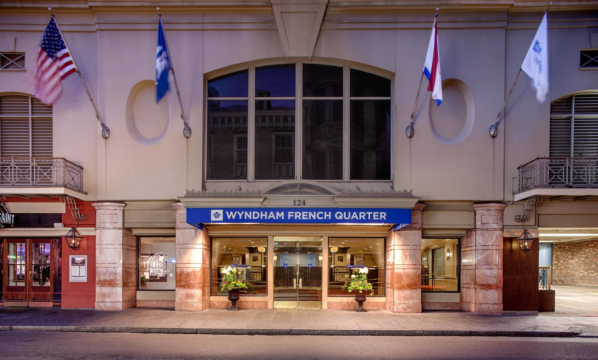 french 桌布 壁紙 — 黃昏時分，Wyndham French Quarter 酒店外牆，旗幟和溫暖的燈光照亮入口。