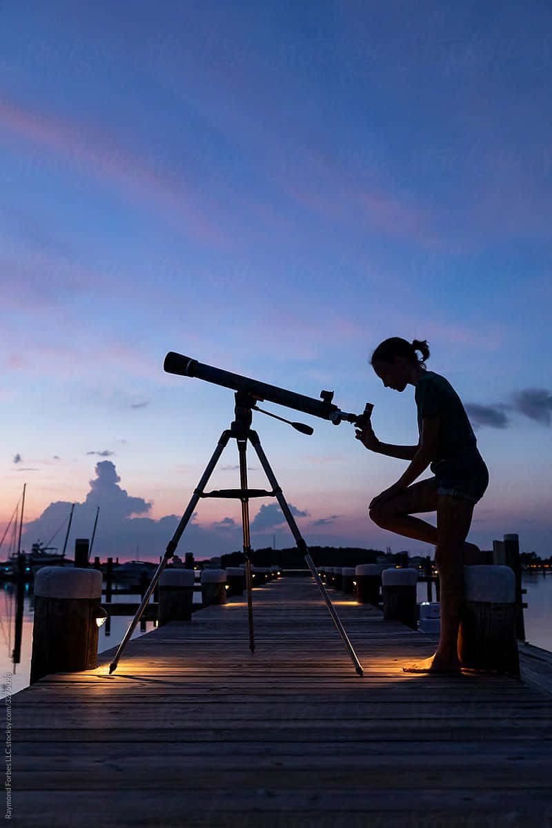 astronomy 桌布 壁紙 — 黃昏時分，一個人在木製碼頭上使用望遠鏡的剪影，天空呈現鮮豔的紫色和藍色。