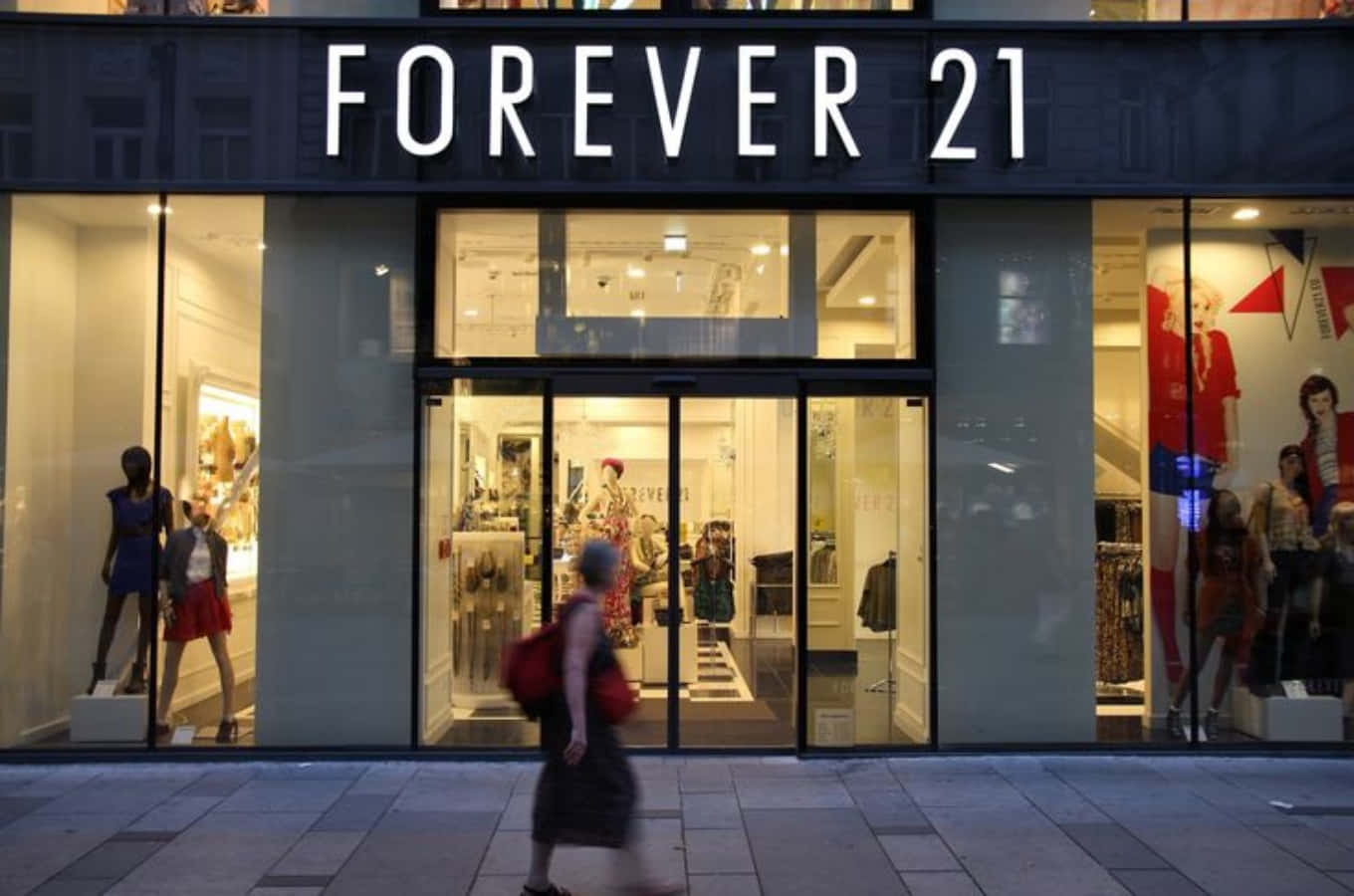 永遠21 桌布 壁紙 — 黃昏時分，一個人走過燈光明亮的Forever 21商店，櫥窗裡的模特兒展示色彩繽紛的服裝。