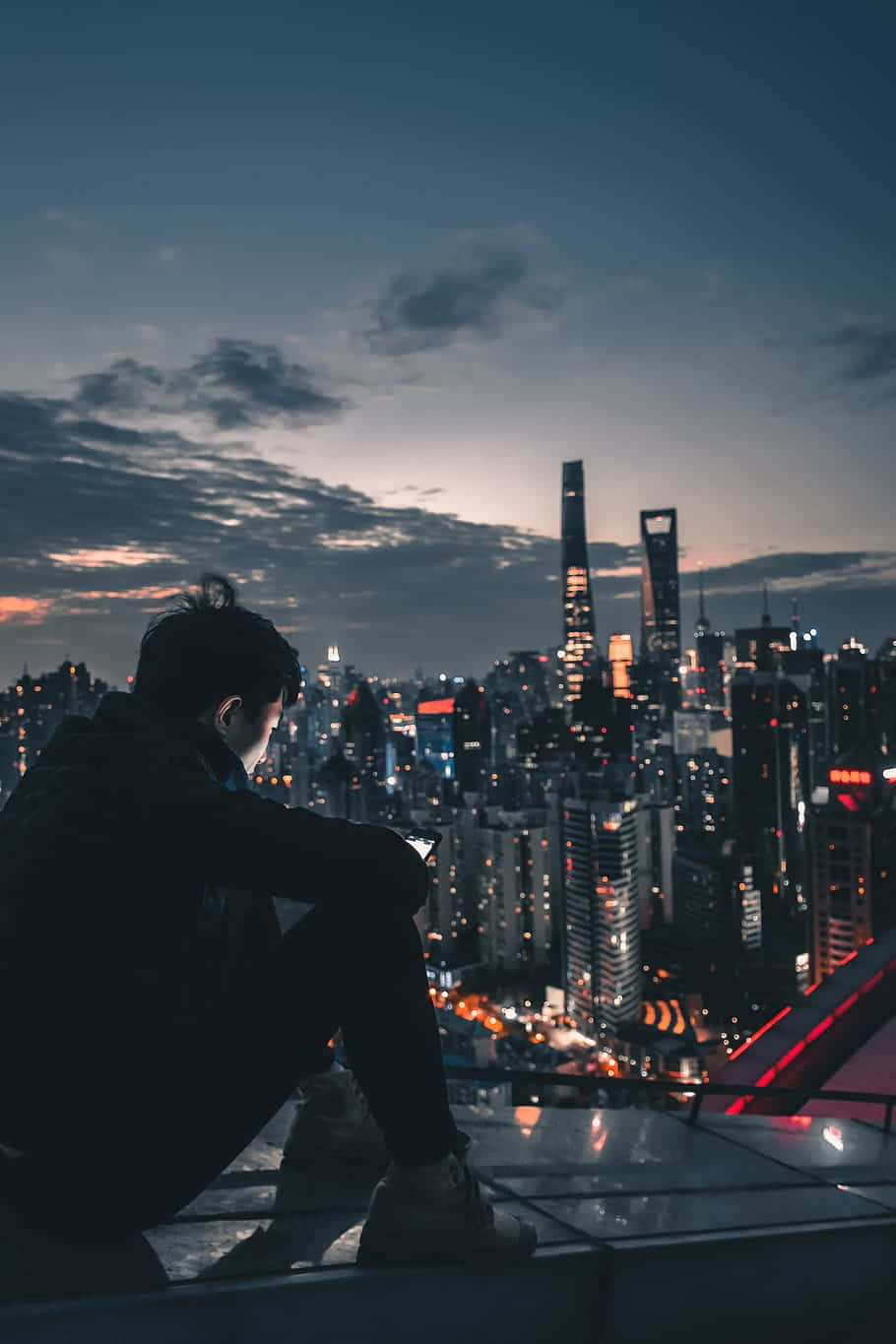 Rooftop 桌布 壁紙 — 黃昏時分，一個孤獨的身影坐在屋頂上，俯瞰著霓虹燈閃爍、高樓林立的廣闊城市景觀。