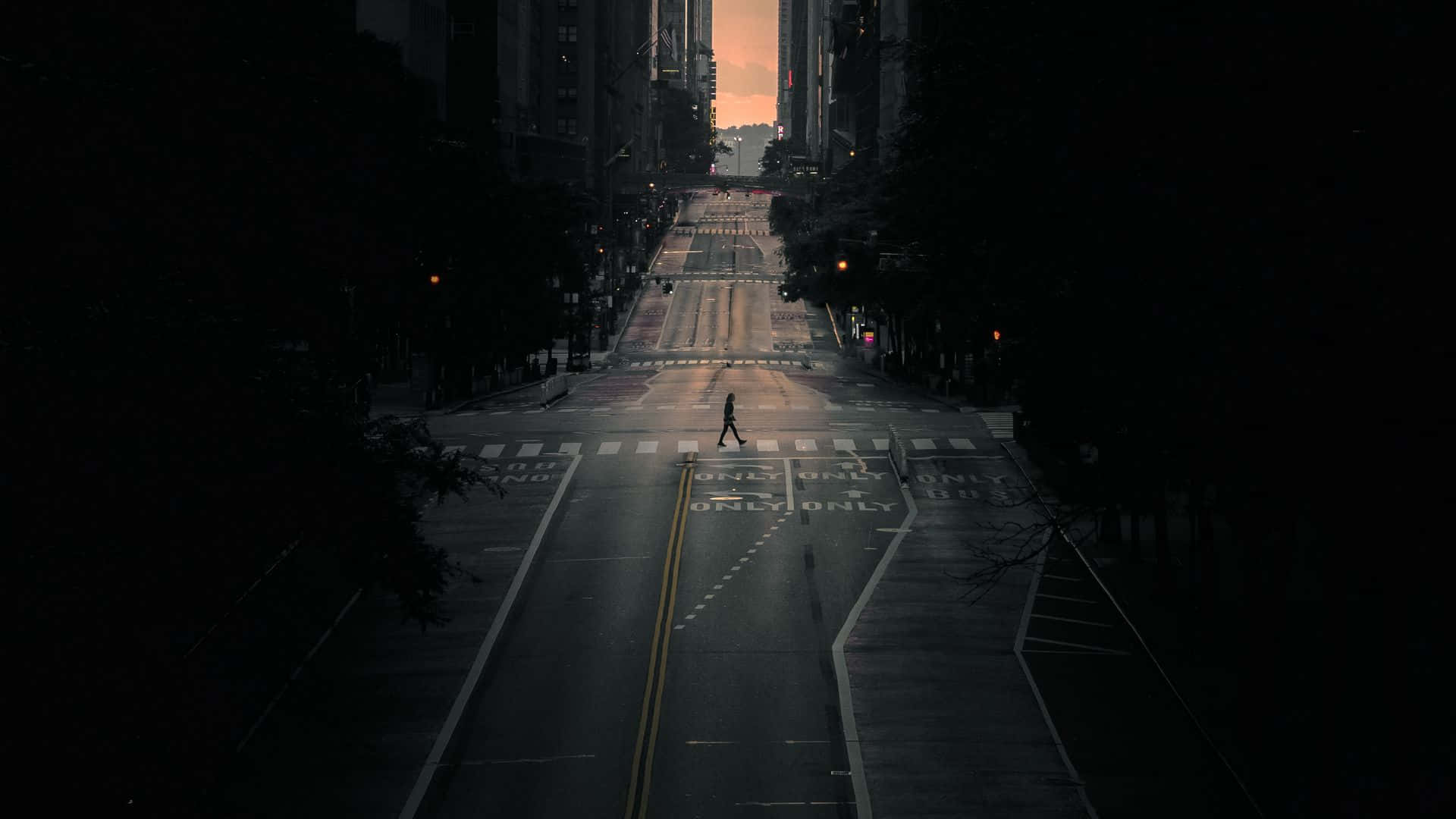 Dark Crossroad 桌布 壁紙 — 黃昏時分，一個孤獨的身影穿過空無一人的城市街道，高聳的建築物框住了發光的地平線。