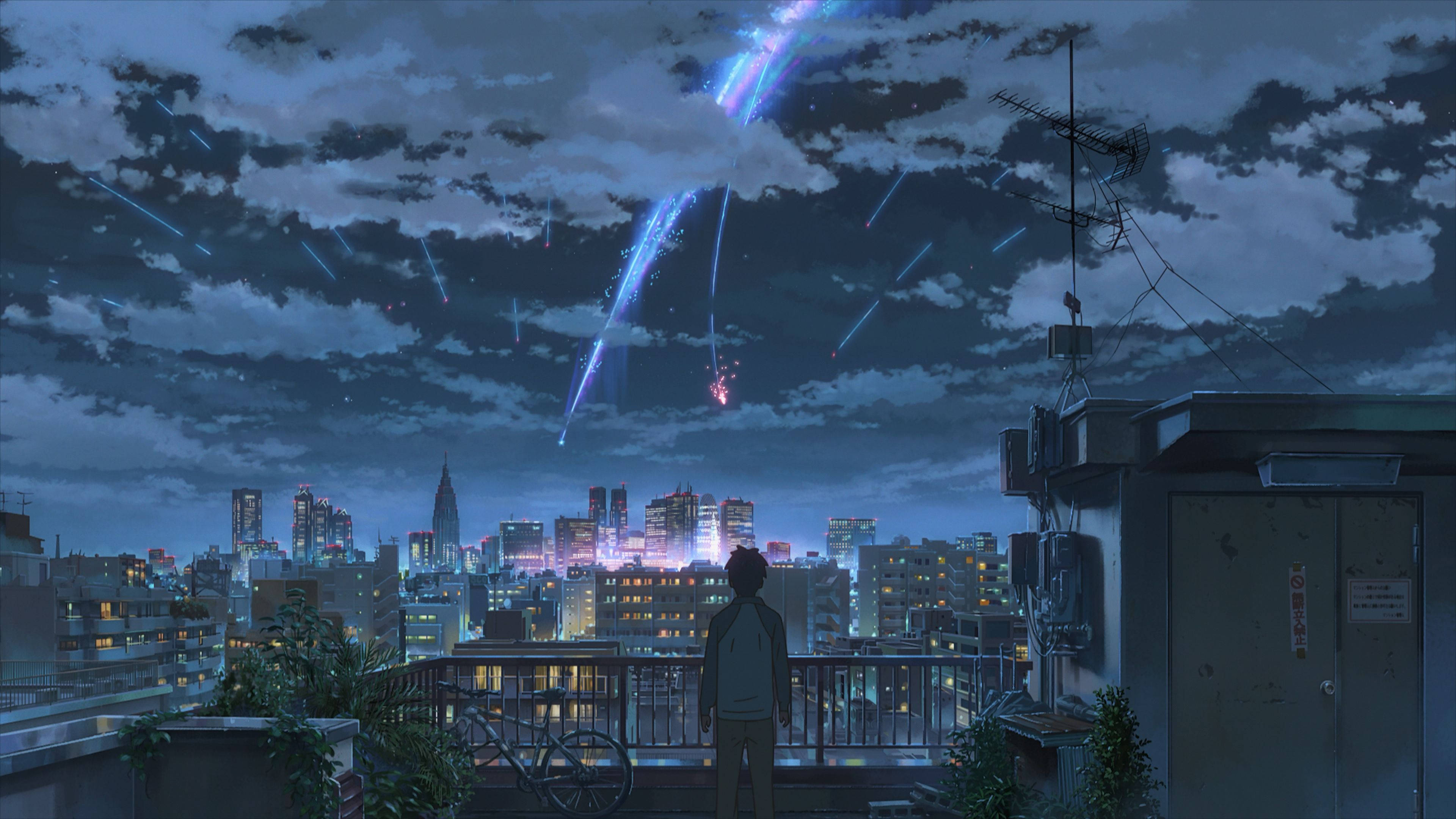 Makoto Shinkai 桌布 壁紙 — 黃昏時分，一個孤獨的身影站在城市屋頂上，觀看鮮豔的藍色和粉紅色流星軌跡劃過多雲的天空，下方是閃爍的城市燈光。