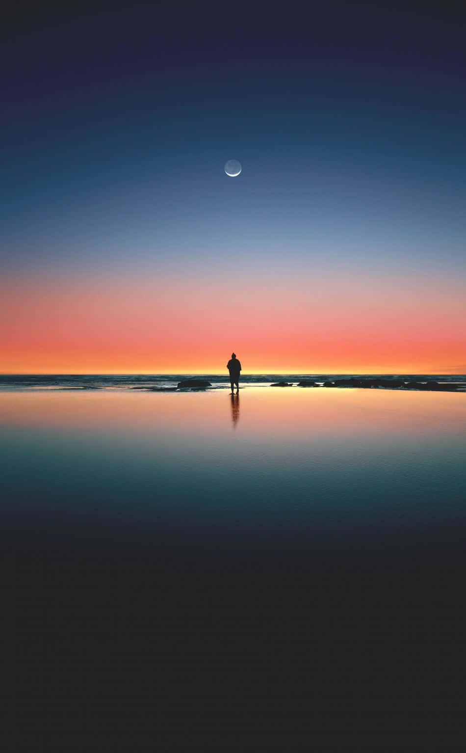 Sunset Beach iPhone 桌布 壁紙 — 黃昏時分，一個孤獨的身影站在濕漉漉的海灘上，一彎新月掛在漸變色的天空中，倒映在平靜的水面上。