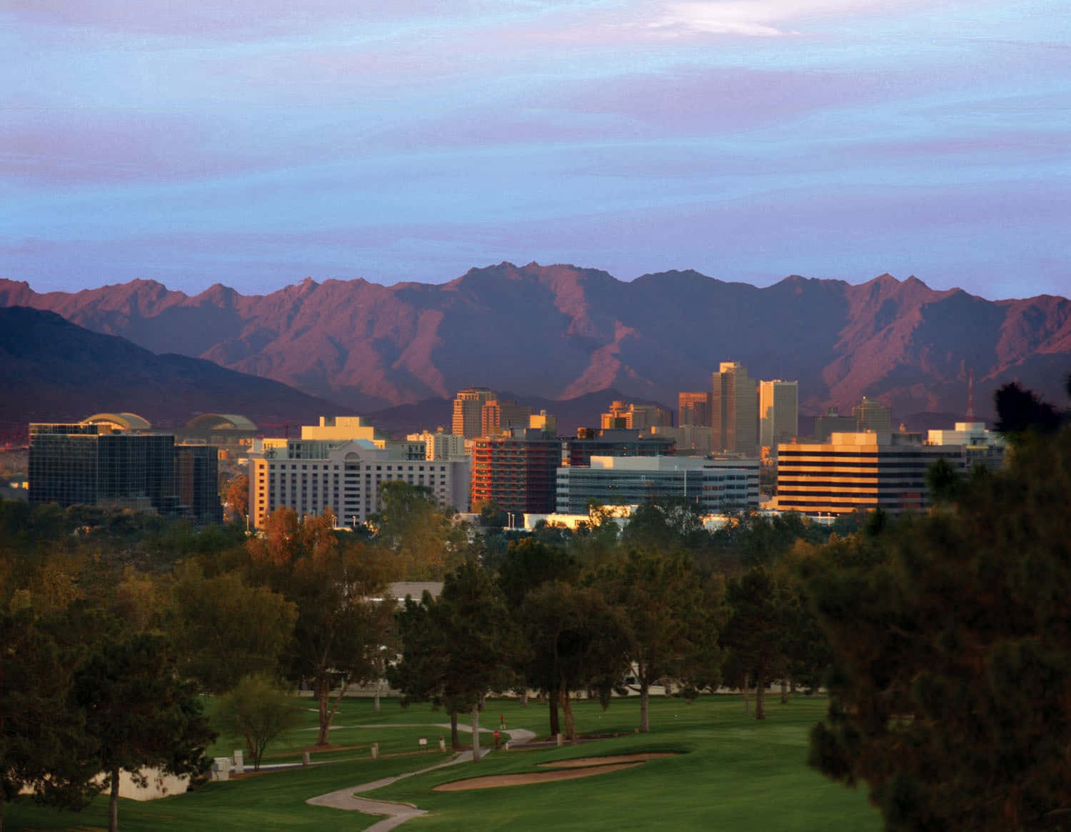Phoenix Arizona 桌布 壁紙 — 黃昏時分，一個寧靜的高爾夫球場前景襯托著城市天際線，背後紫色山巒閃耀。