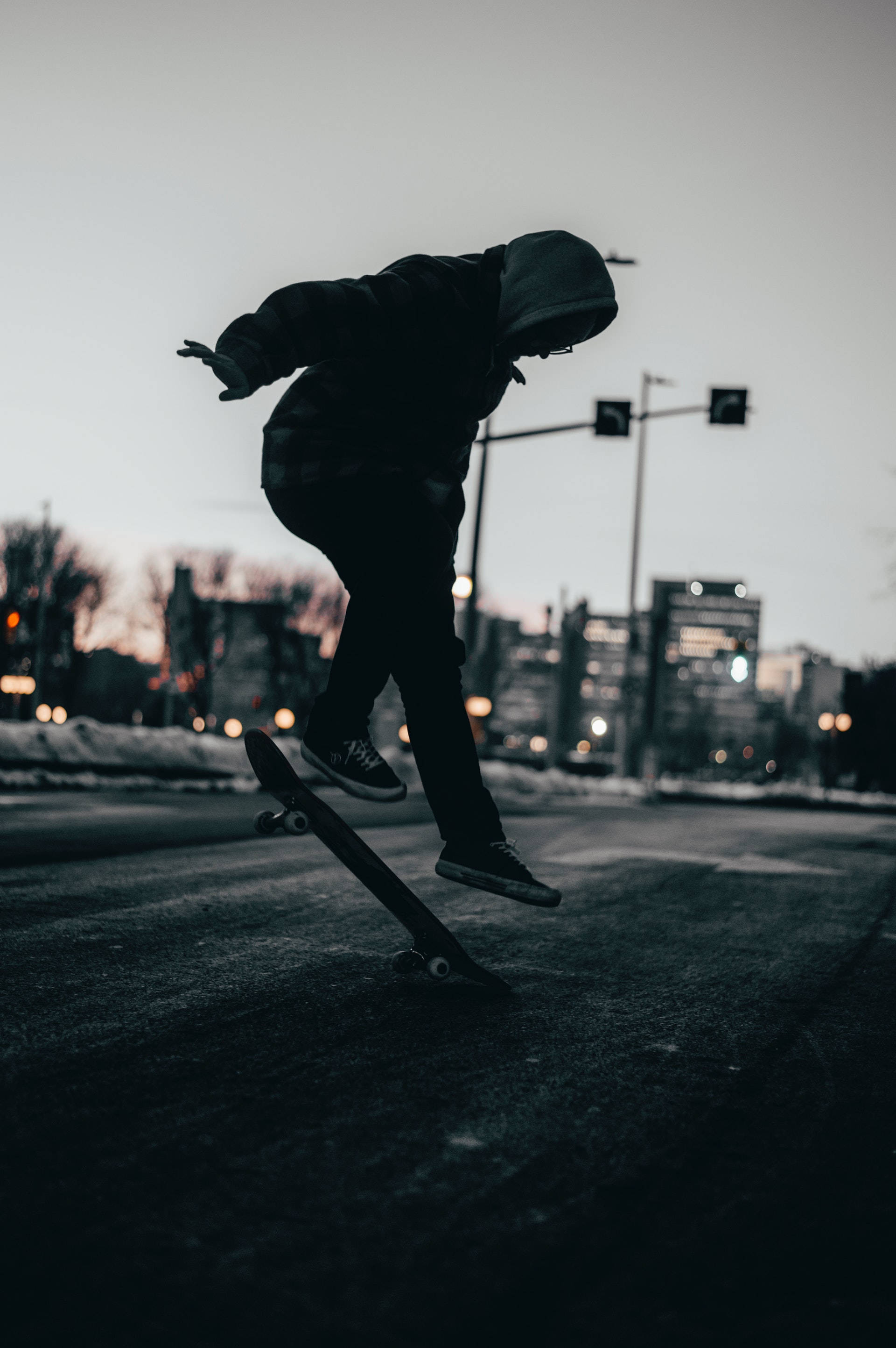 Skater Boy 桌布 壁紙 — 黃昏時分，一名滑板手在城市街道上進行特技的剪影，背景是模糊的城市燈光。
