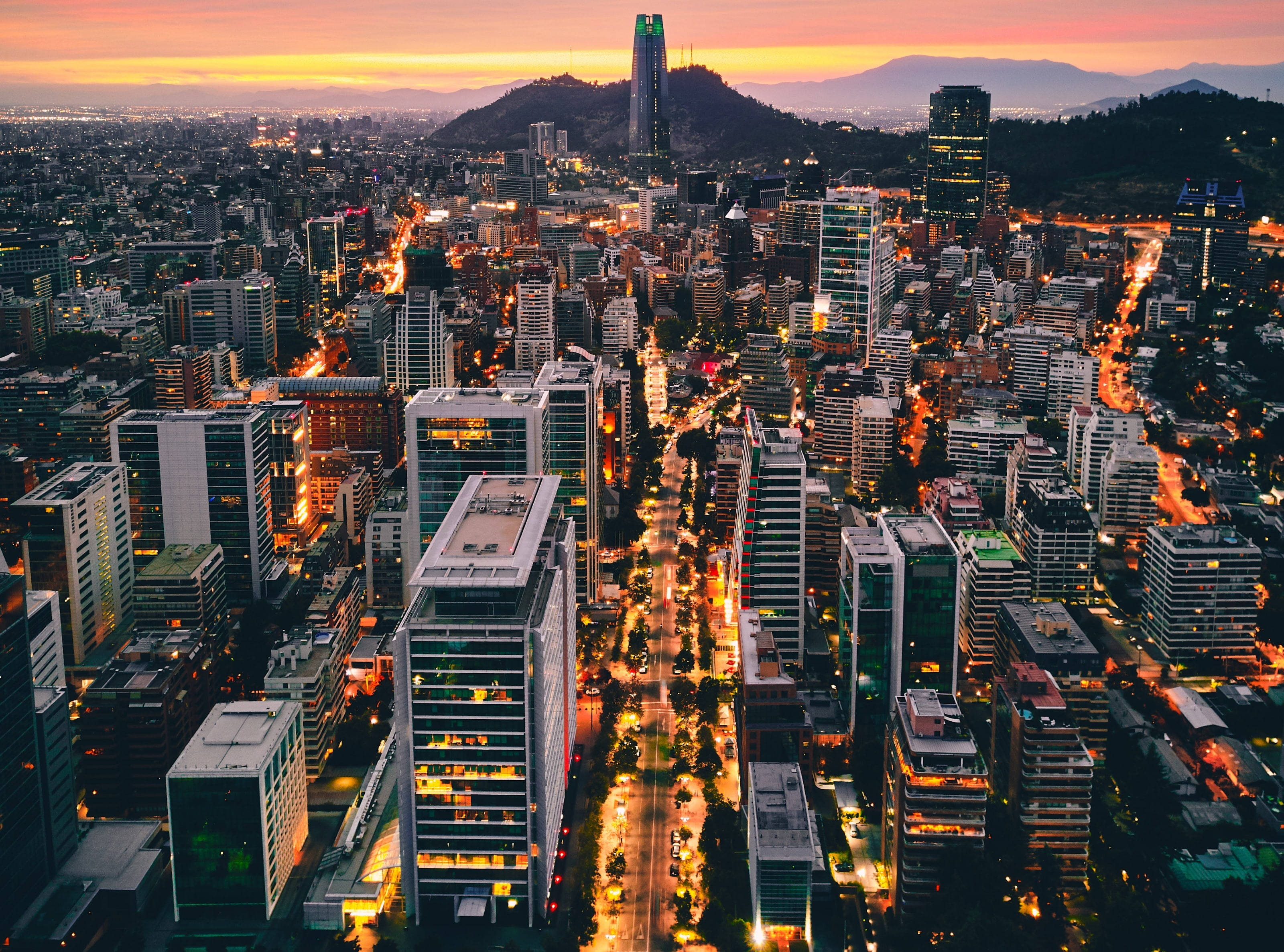 Chile 桌布 壁紙 — 黃昏時分，一座廣闊城市的鳥瞰圖，發光的街道和高聳的摩天大樓映襯著火紅的橙色天空。