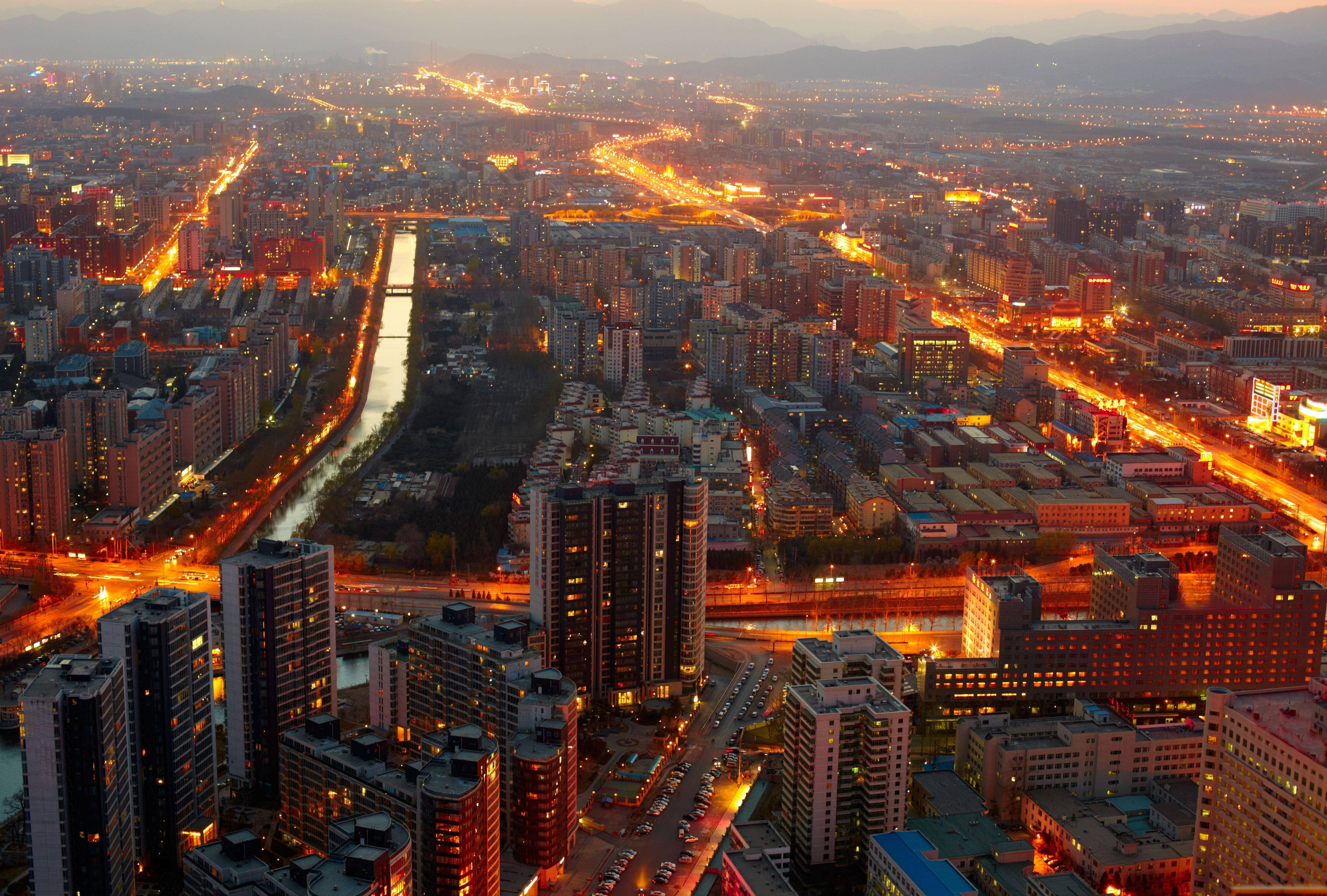Beijing 桌布 壁紙 — 黃昏時分，一座廣闊城市的鳥瞰圖，發光的街道和建築物在漸暗的天空下熠熠生輝。