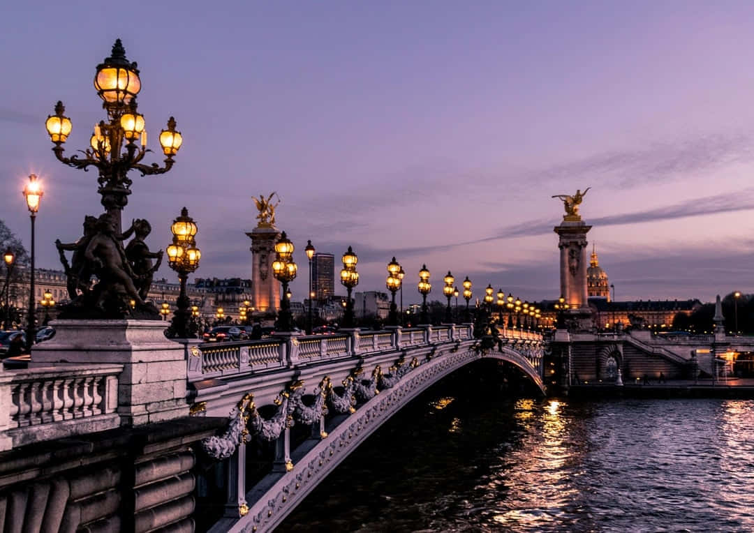 Paris Aesthetic 桌布 壁紙 — 黃昏時分，一座華麗的大橋橫跨河流，發光的街燈和雕像映襯著紫色的天空。