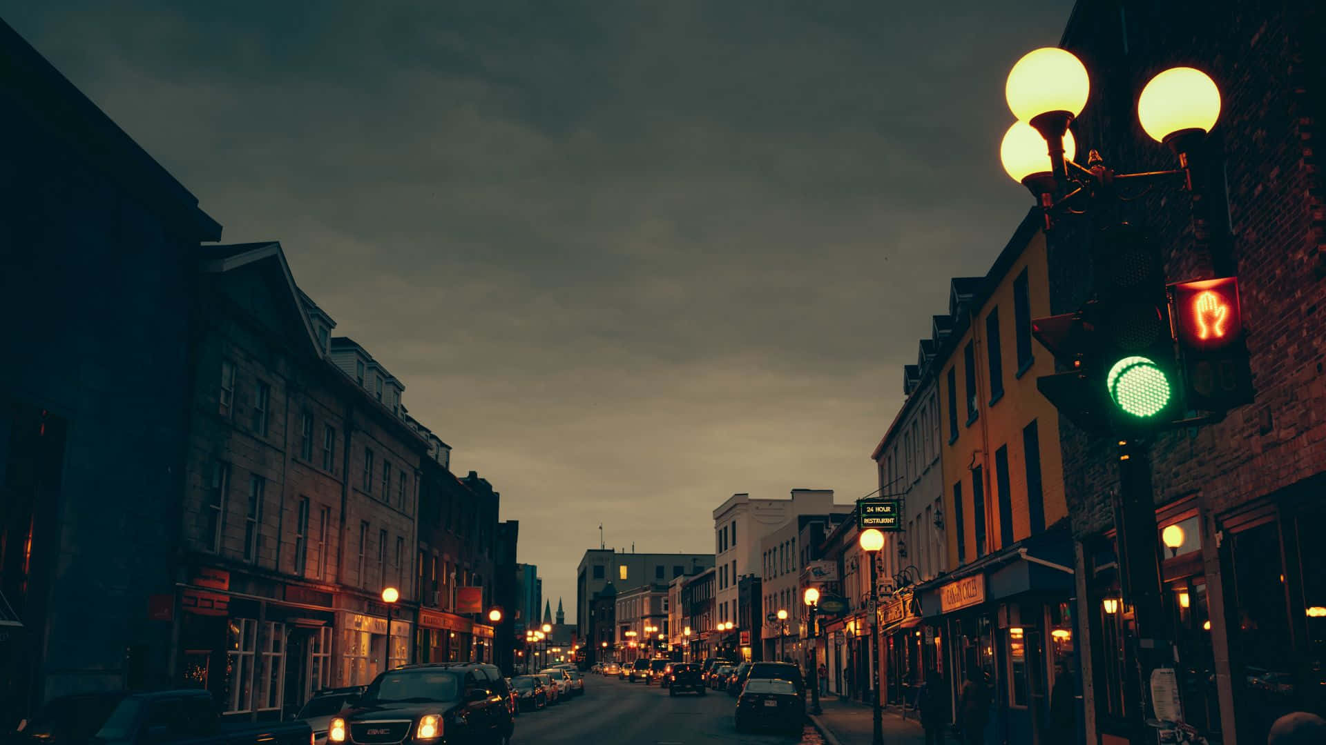Night Street 桌布 壁紙 — 黃昏時分，一條燈光昏暗的城市街道，亮著的路燈和紅色的行人信號燈映襯著陰鬱的天空。