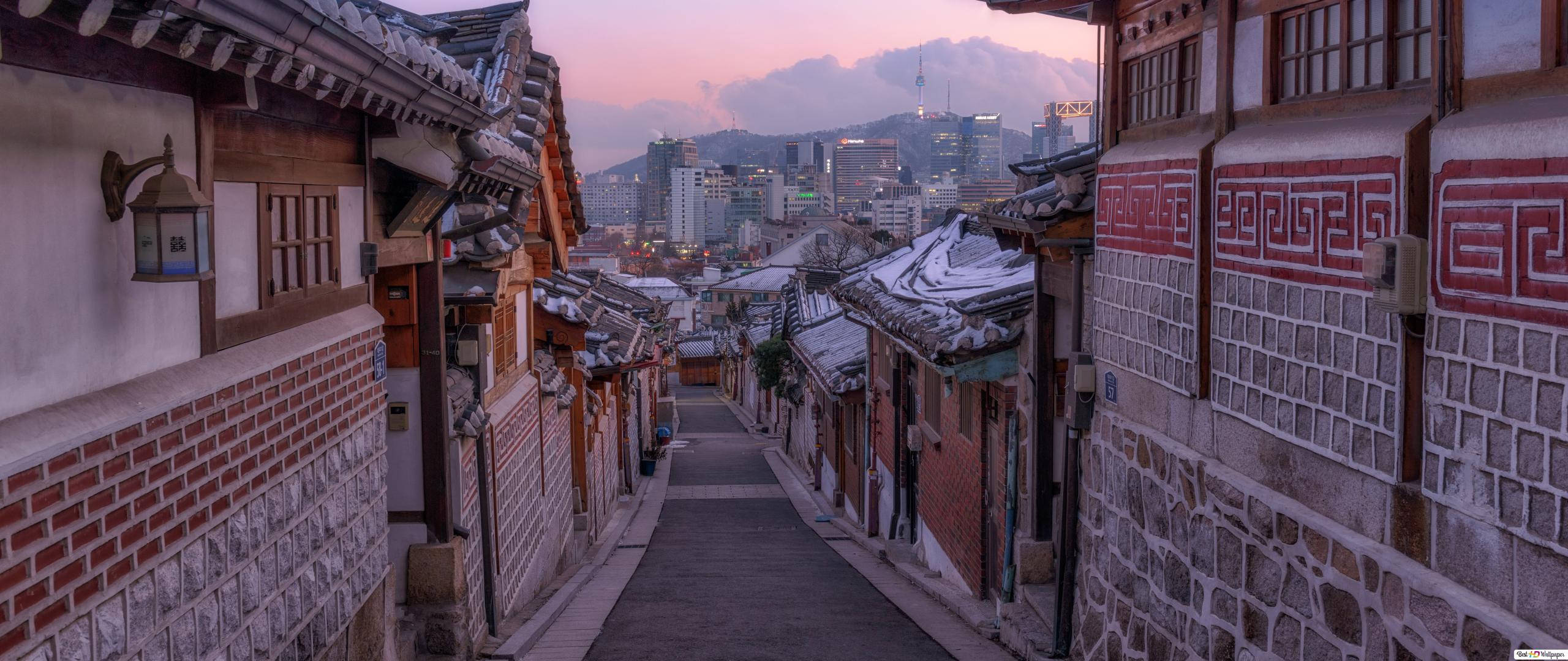 Asia 桌布 壁紙 — 黃昏時分，一條積雪的傳統韓國小巷，遠處是現代城市天際線。