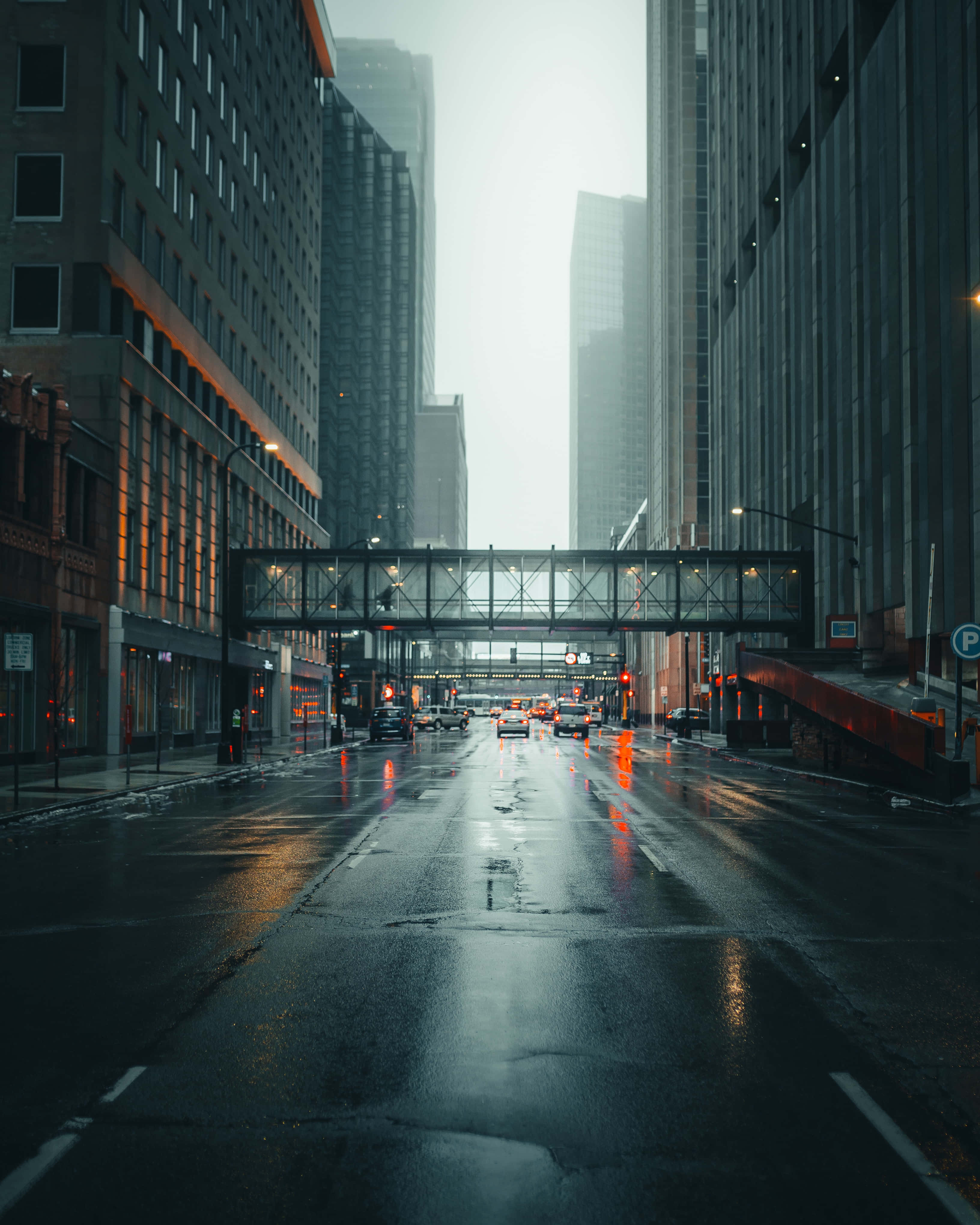 City Street 桌布 壁紙 — 黃昏時分，一條被雨水打濕的城市街道，高聳的建築物、發光的街燈和頭頂上的行人天橋。