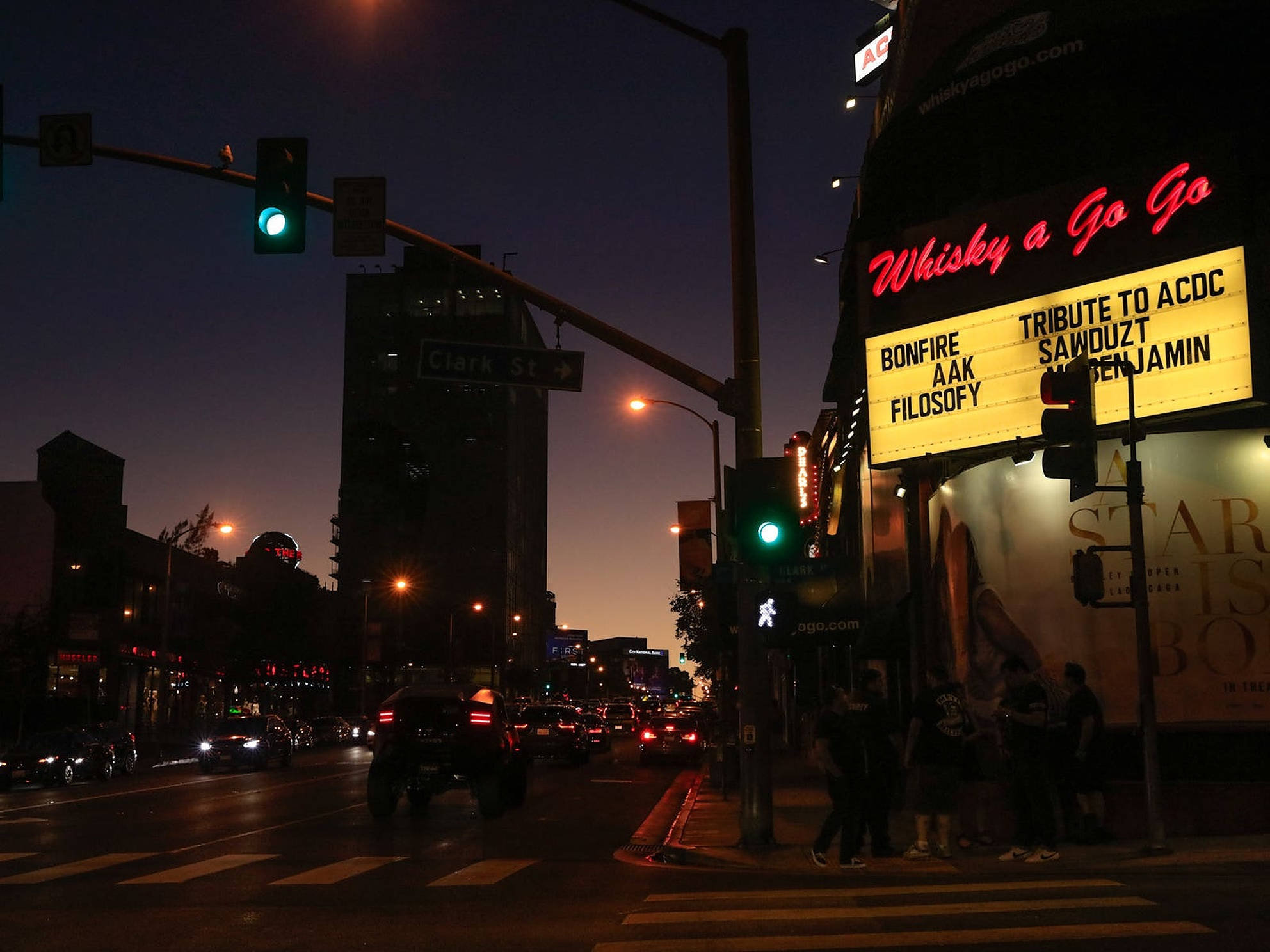 Boulevard 桌布 壁紙 — 黃昏時分，一條霓虹燈照亮的城市街道，發光的「Whisky a Go Go」招牌和交通燈在濕漉漉的路面上投射出溫暖的光芒。