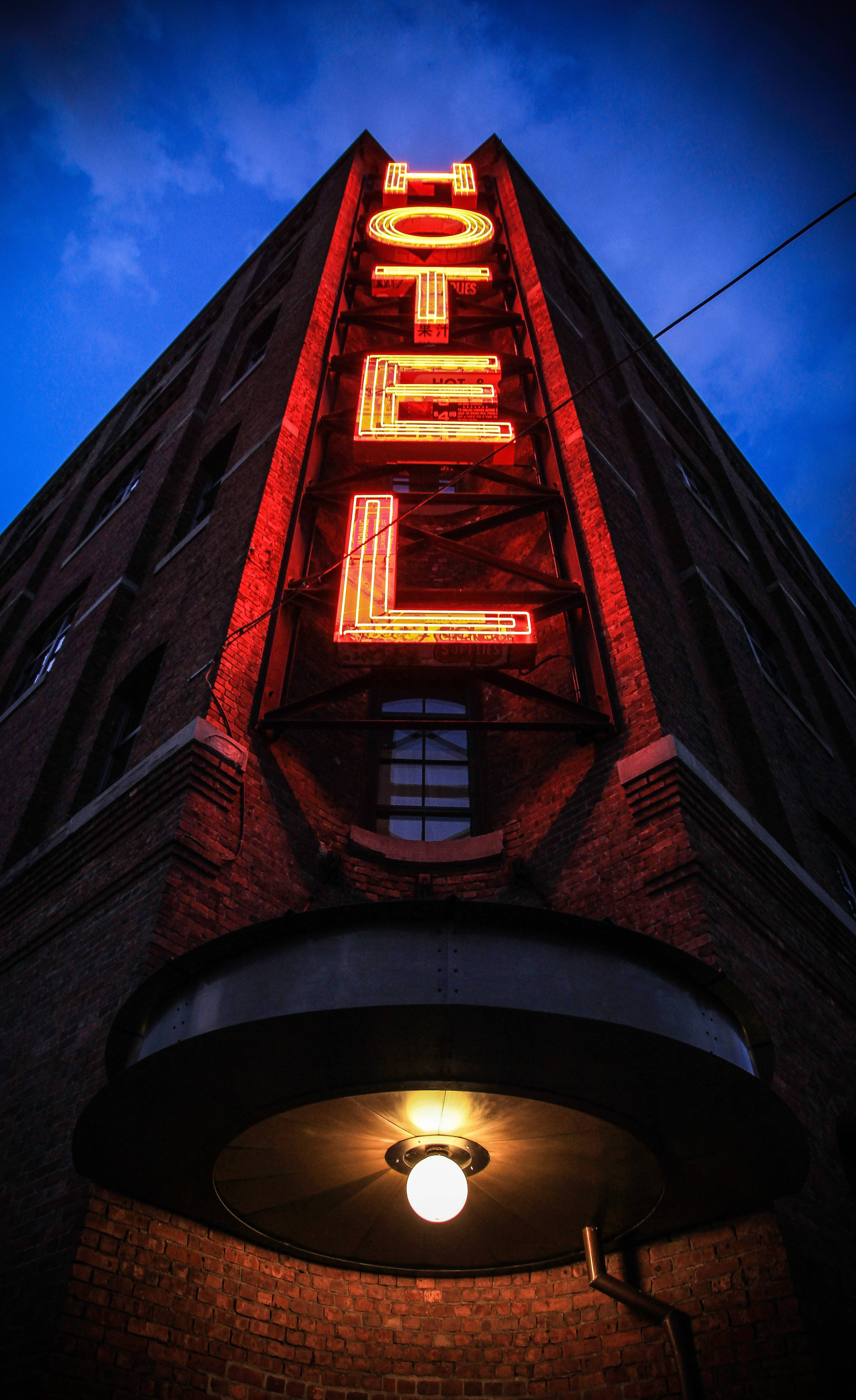 Hotel 桌布 壁紙 — 黃昏時分，以低角度拍攝的磚砌酒店建築，帶有發光的紅色霓虹燈招牌和溫暖的頭頂燈光。
