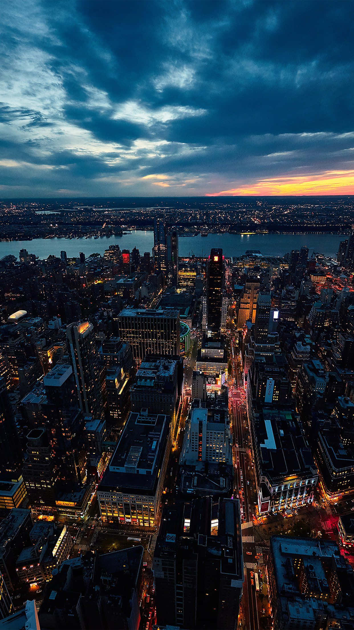 manhattan 桌布 壁紙 — 黃昏時分，俯瞰一座廣闊的城市，閃爍的摩天大樓和水面上充滿活力的橙色地平線。