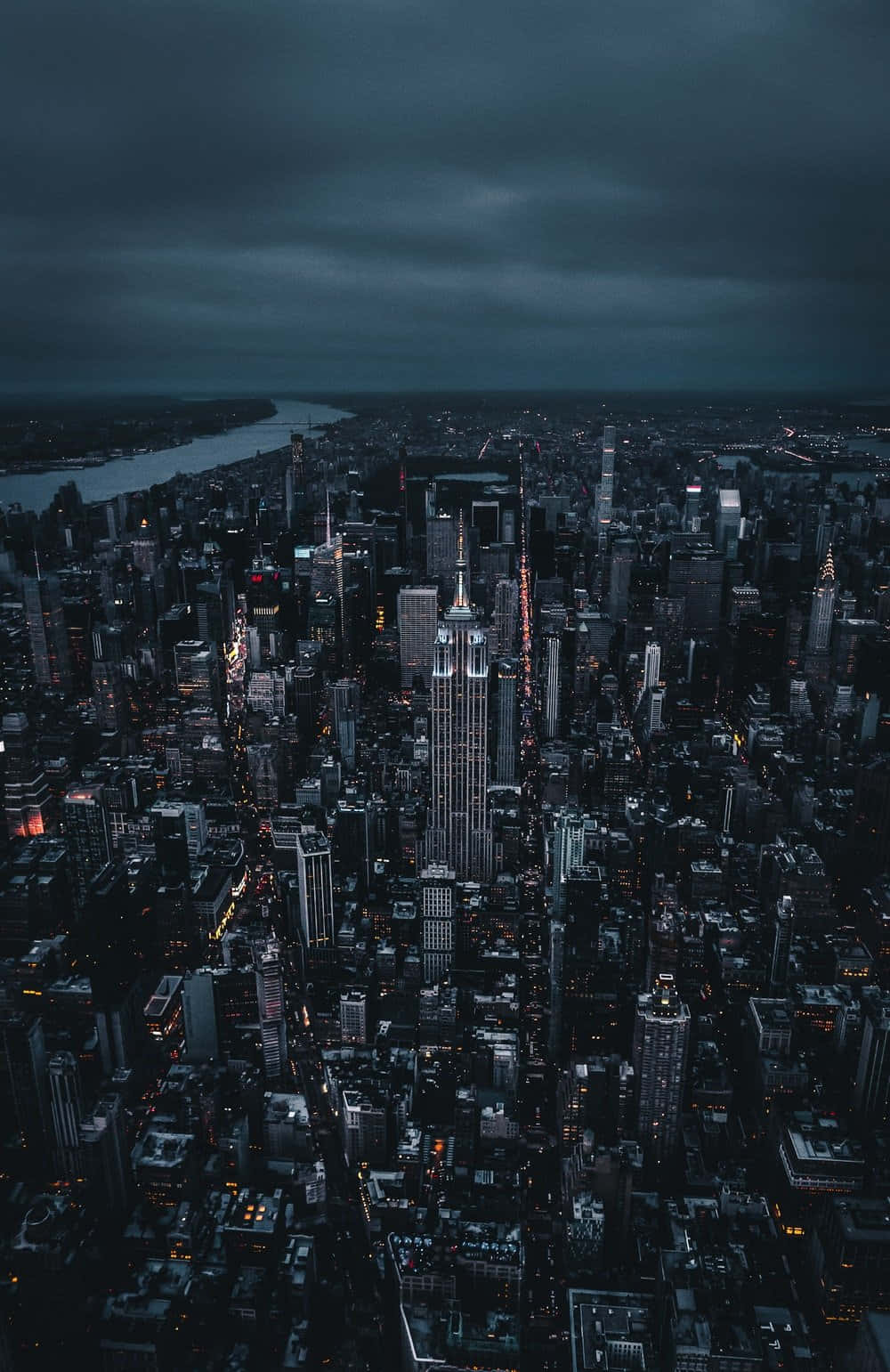 紐約市 桌布 壁紙 — 黃昏時分，在陰暗多雲的天空下，廣闊的城市景觀鳥瞰圖，高聳的摩天大樓和發光的街燈。