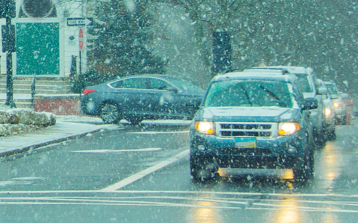 Winter Driving 桌布 壁紙 — 黃昏時分，大雪紛飛，雪花翻騰，汽車開著車頭燈在濕漉漉的城市街道上行駛。