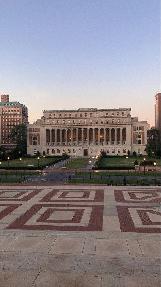 Library 桌布 壁紙 — 黃昏時分，宏偉的新古典主義大學建築，配有發光的柱子和幾何磚砌廣場。