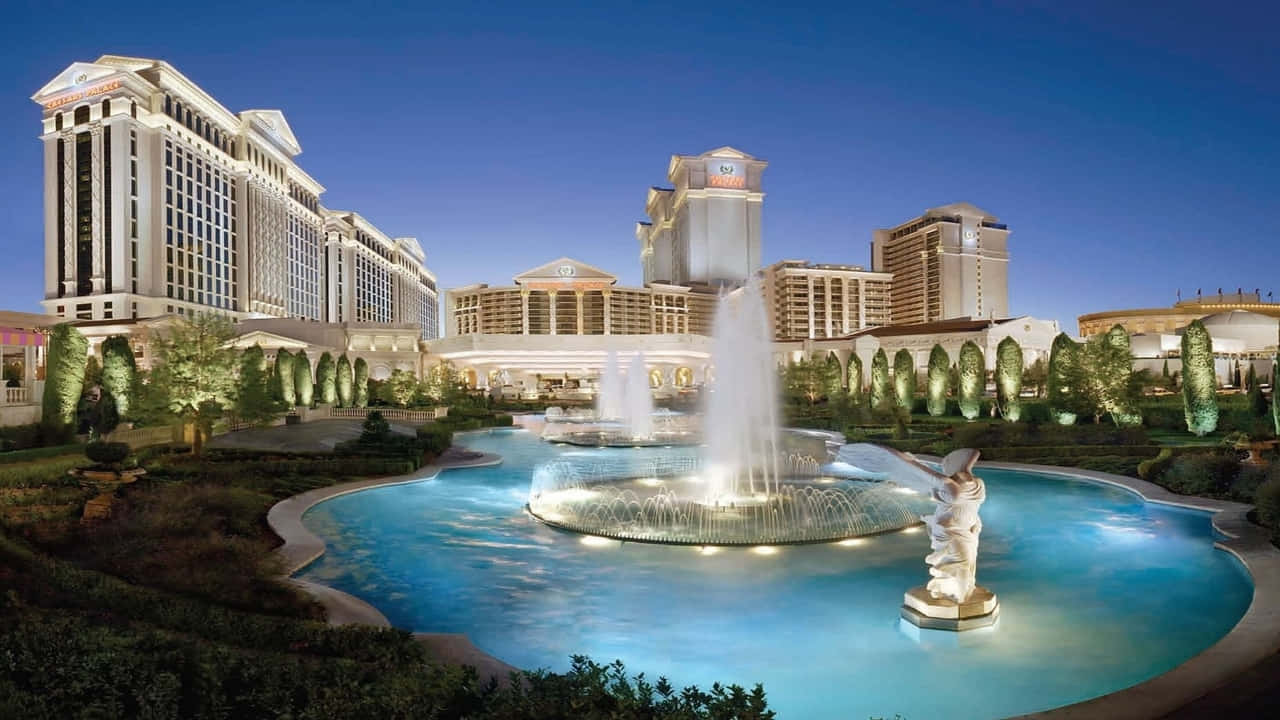 720p Las Vegas 桌布 壁紙 — 黃昏時分，宏偉的燈光飯店綜合體，前景有發光的噴泉和雕像。