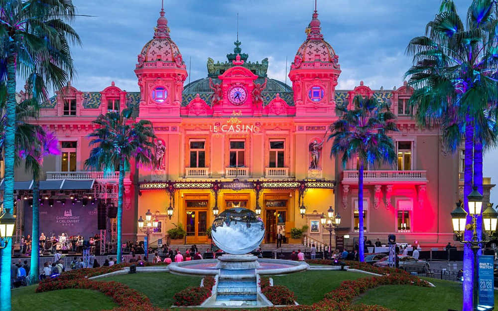 Casino 桌布 壁紙 — 黃昏時分，巨大的粉紅色賭場建築亮起燈光，前景有棕櫚樹和反射的噴泉。