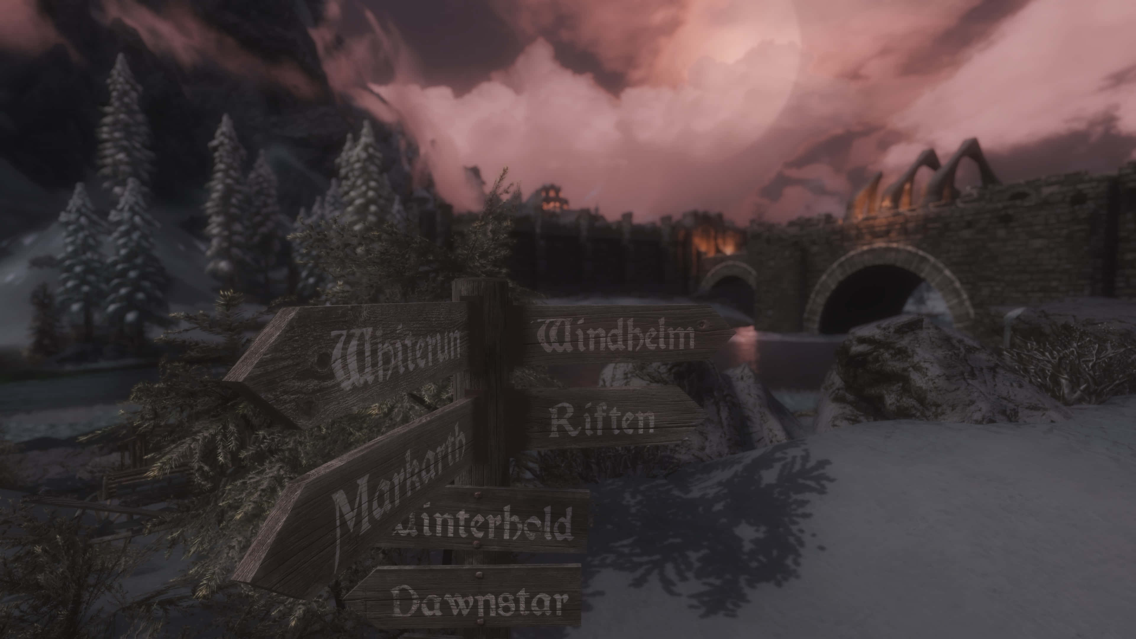 Skyrim Windhelm 桌布 壁紙 — 黃昏時分，幻想村莊中一個被雪覆蓋的木製路標，背景有巨大的月亮和石橋。