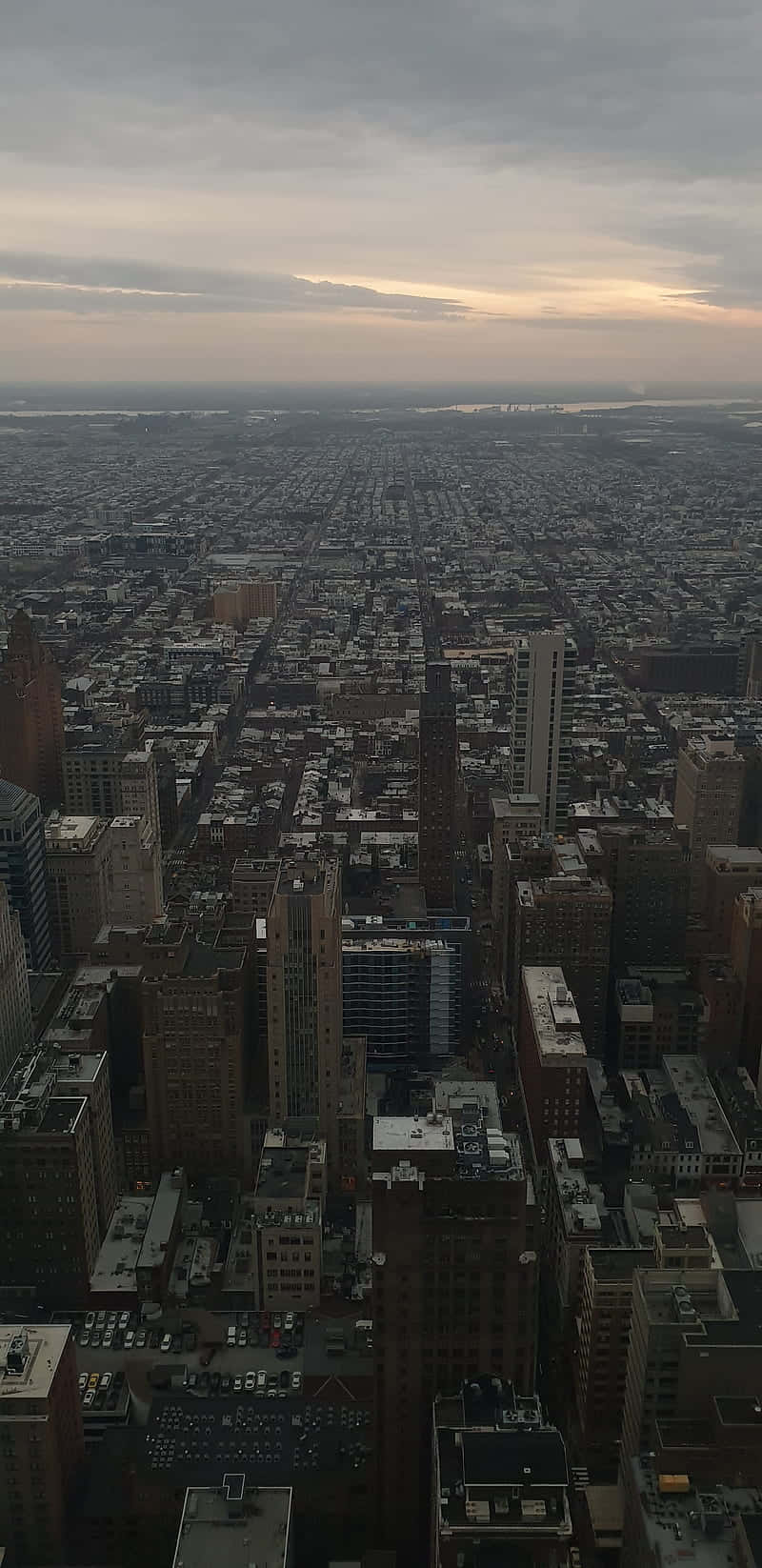 Philly 桌布 壁紙 — 黃昏時分，從空中俯瞰廣闊的城市景觀，高聳的建築物和密集的街道在陰雲密佈的天空下延伸。