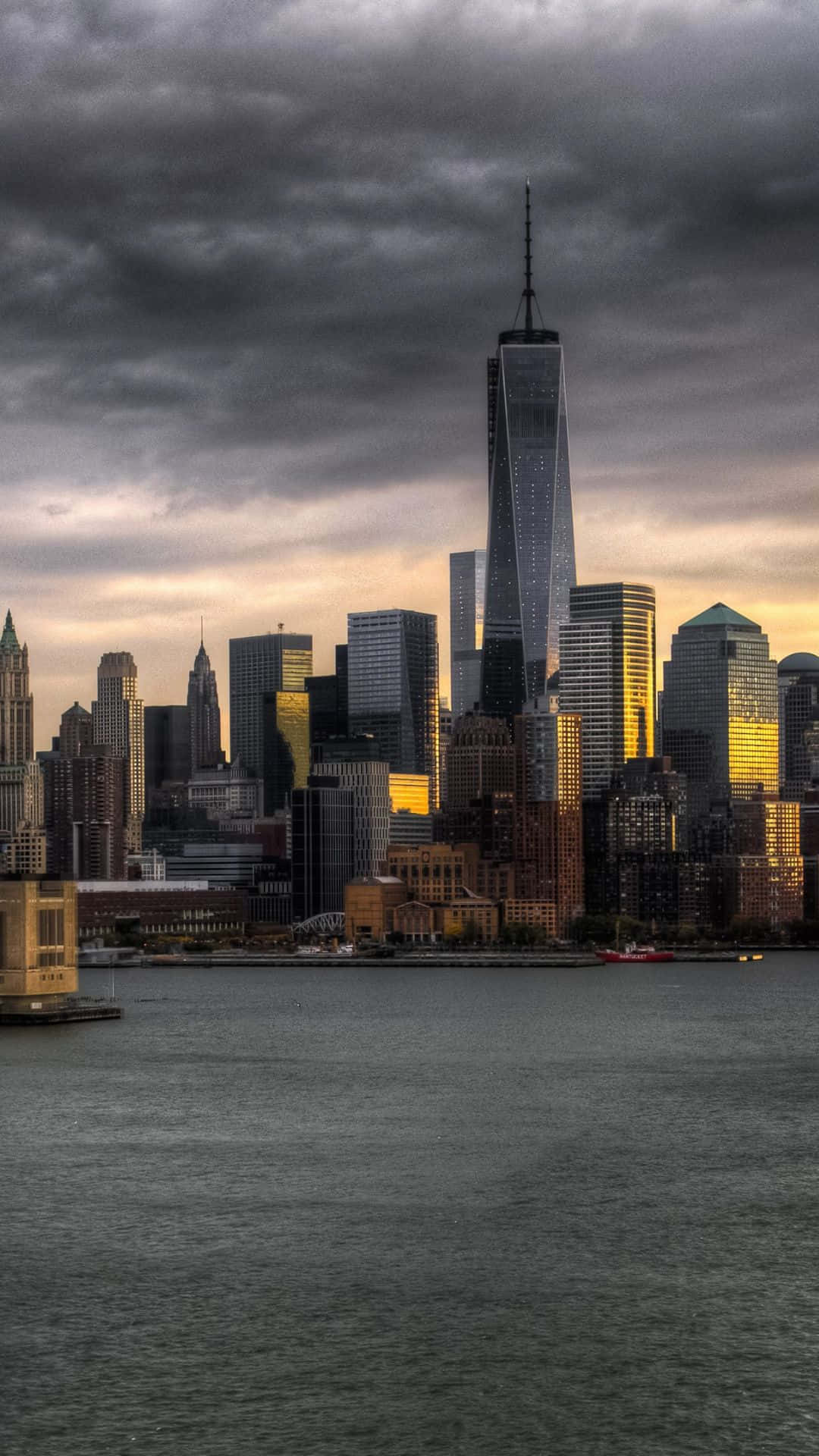 Android Ny City 桌布 壁紙 — 黃昏時分，摩天大樓天際線在暴風雲下，金色光線反射在玻璃塔上，場面戲劇化。