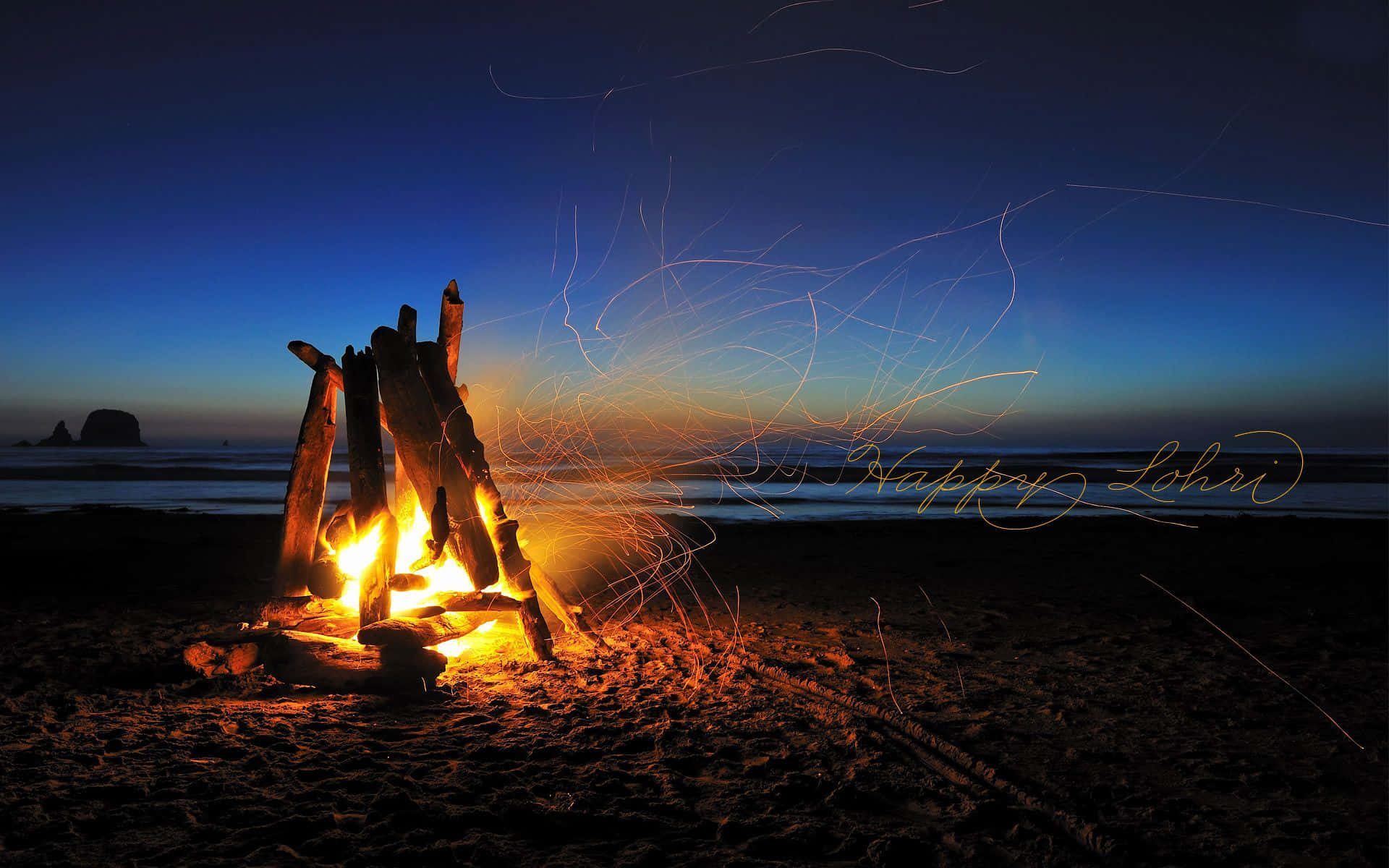 Fall Bonfire 桌布 壁紙 — 黃昏時分，沙灘上噼啪作響的營火，餘燼閃爍，遠方海岩在深藍天空下若隱若現。