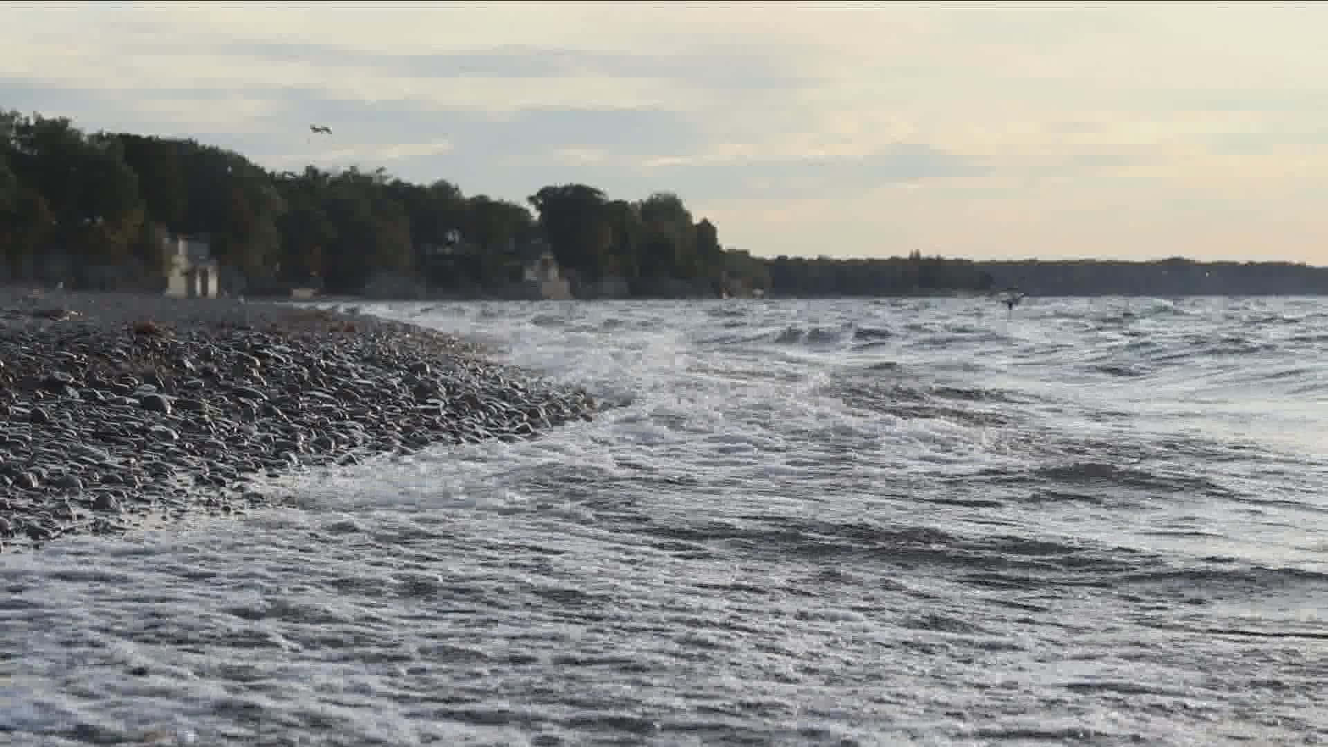 Lake Erie 桌布 壁紙 — 黃昏時分，海浪拍打岩石海岸線，樹木和遠處的房屋沿著水邊。