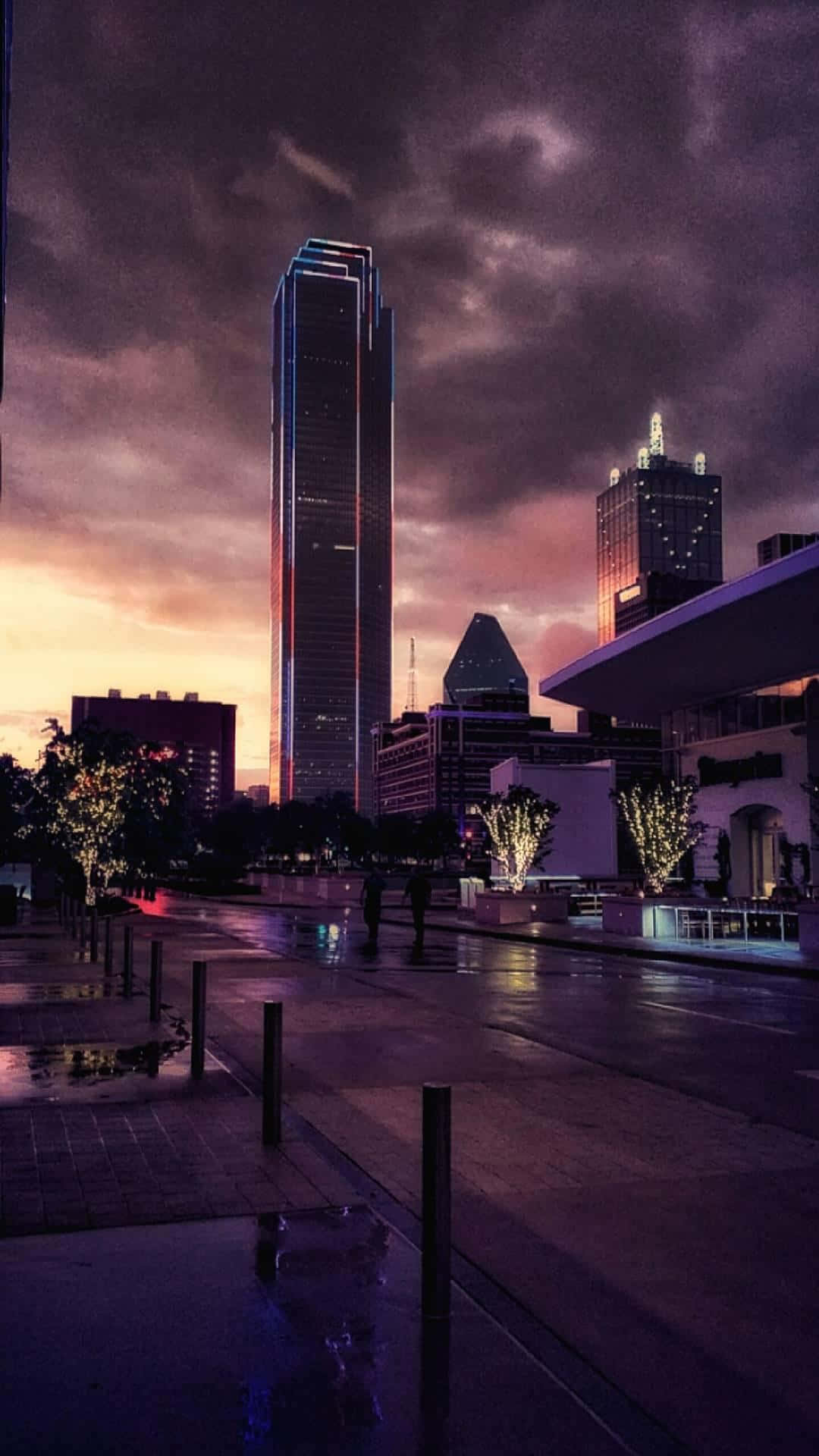 Dallas Skyline 桌布 壁紙 — 黃昏時分，濕漉漉的城市街道在戲劇性的紫色和橙色天空下反射著霓虹燈光，高聳的摩天大樓林立。