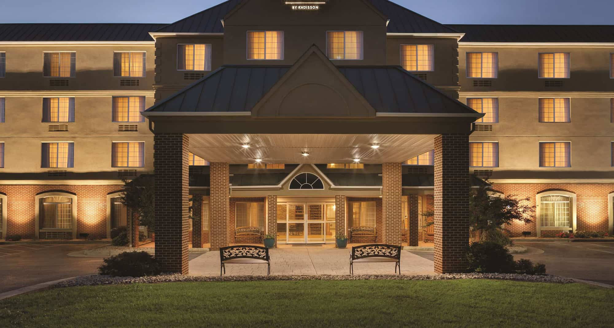 Hotel 桌布 壁紙 — 黃昏時分，燈光溫暖的酒店建築，窗戶發光，有蓋入口兩側設有長椅。