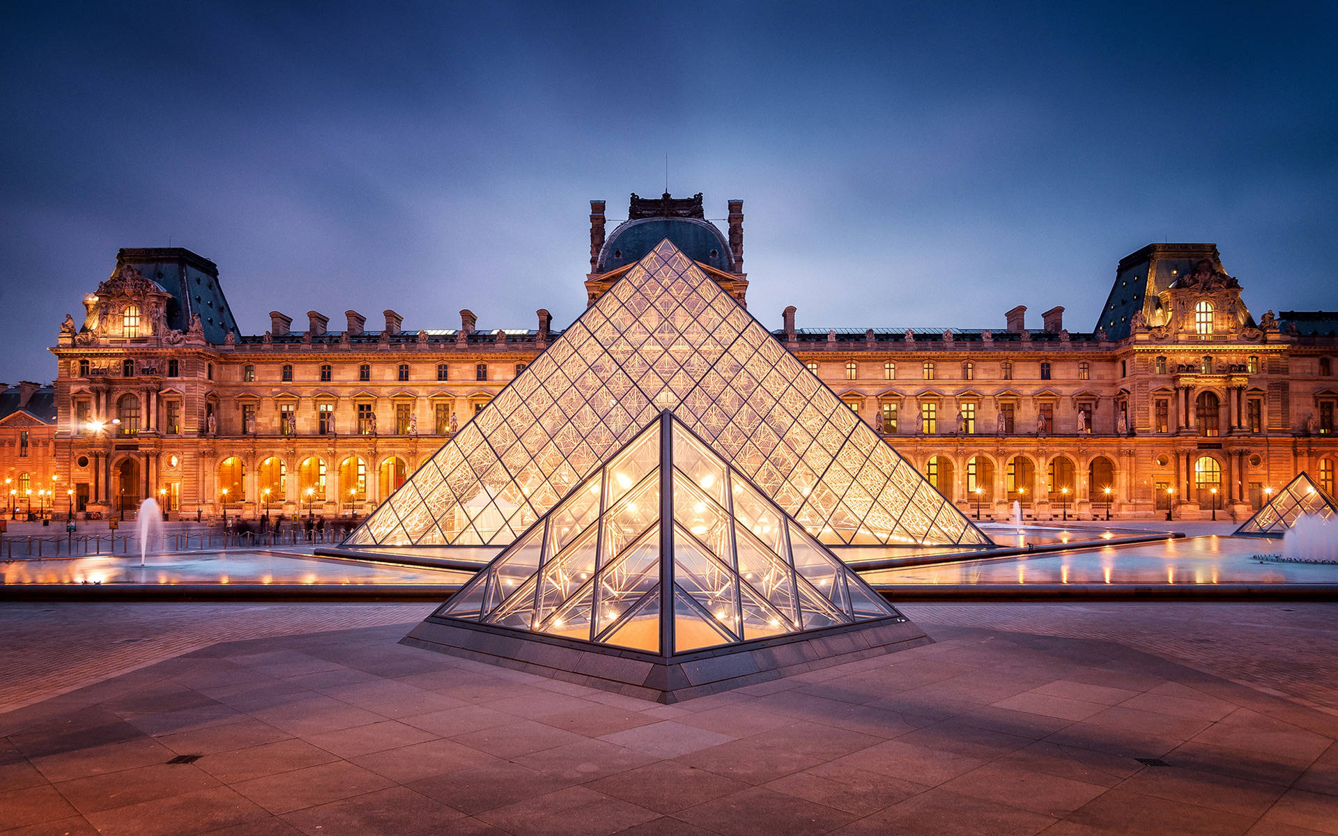France 桌布 壁紙 — 黃昏時分，發光的玻璃金字塔倒映在噴泉中，背景是宏偉的新古典主義羅浮宮博物館立面。