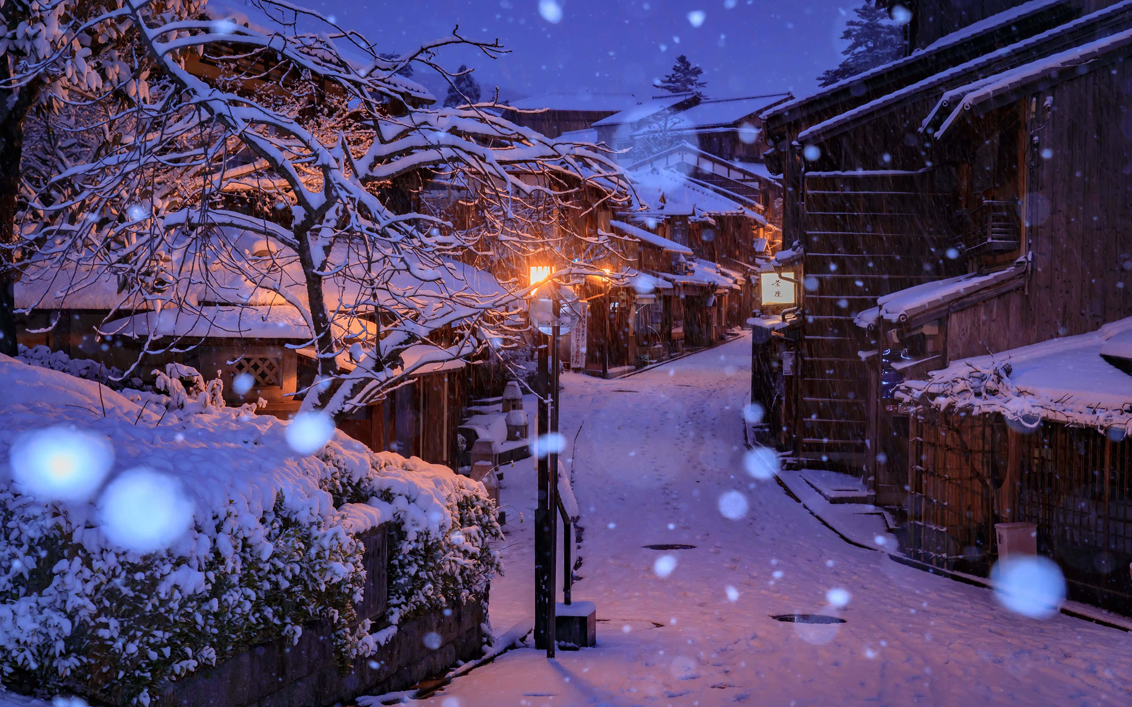 冬天 桌布 壁紙 — 黃昏時分，白雪覆蓋寧靜的村莊小巷，溫暖的燈籠光在寒冷的藍色暮色中閃耀。