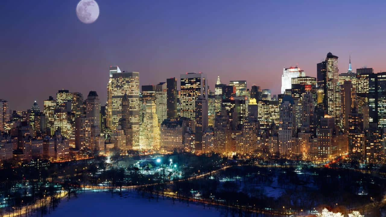 720p Ny City 桌布 壁紙 — 黃昏時分，白雪覆蓋的城市天際線，一輪滿月在燈火通明的摩天大樓和中央公園上方閃耀。