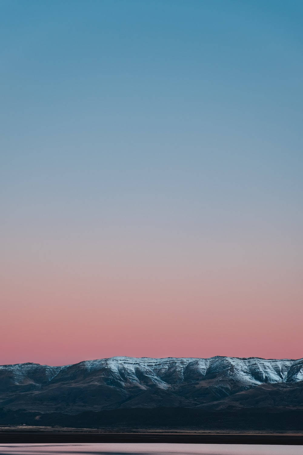 View 桌布 壁紙 — 黃昏時分，白雪覆蓋的山峰在藍粉漸變的天空中形成剪影。