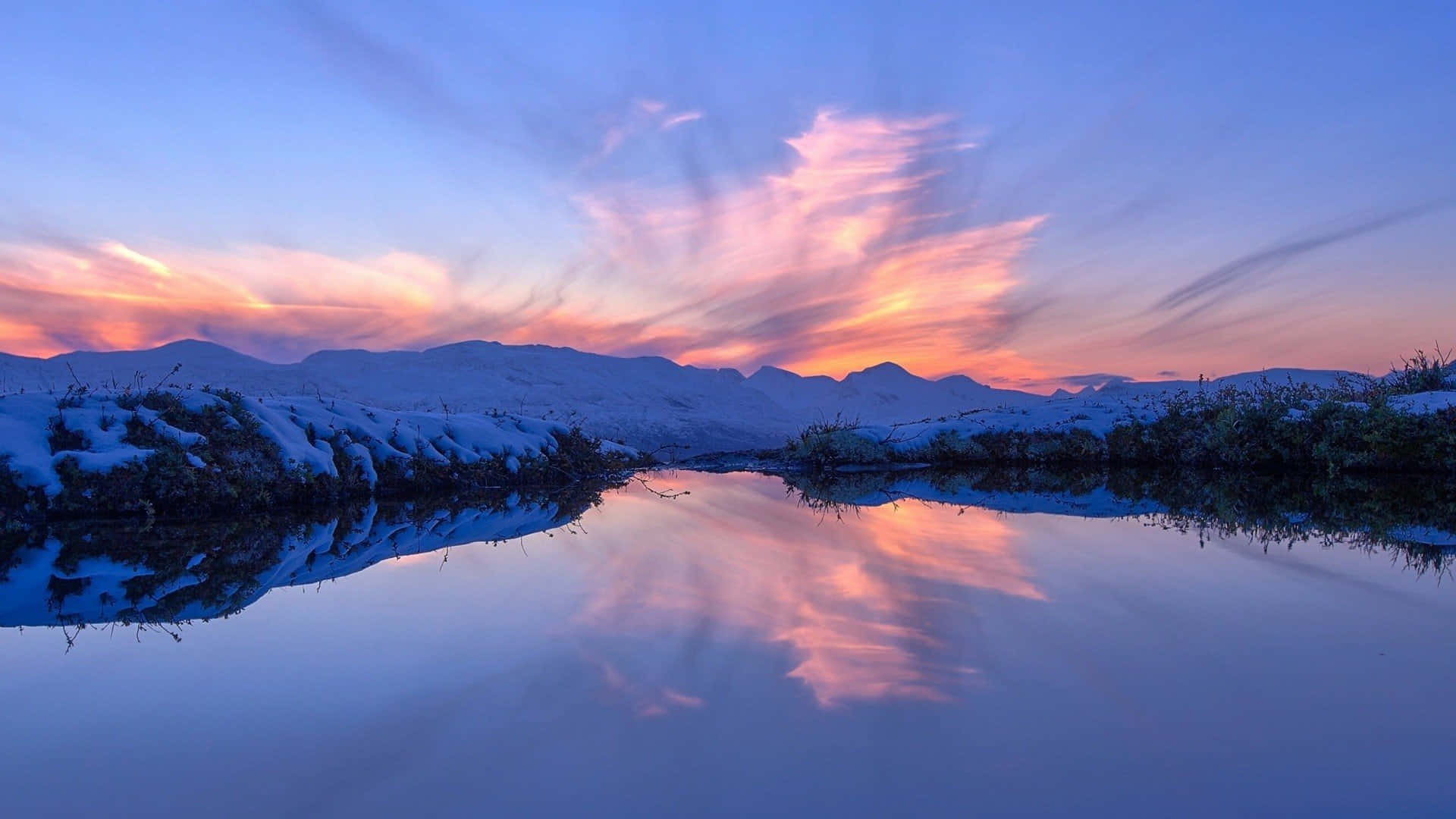 Sunset Aesthetic 桌布 壁紙 — 黃昏時分，白雪覆蓋的風景，充滿活力的粉紅色和橙色雲彩倒映在平靜的冰凍湖面上。