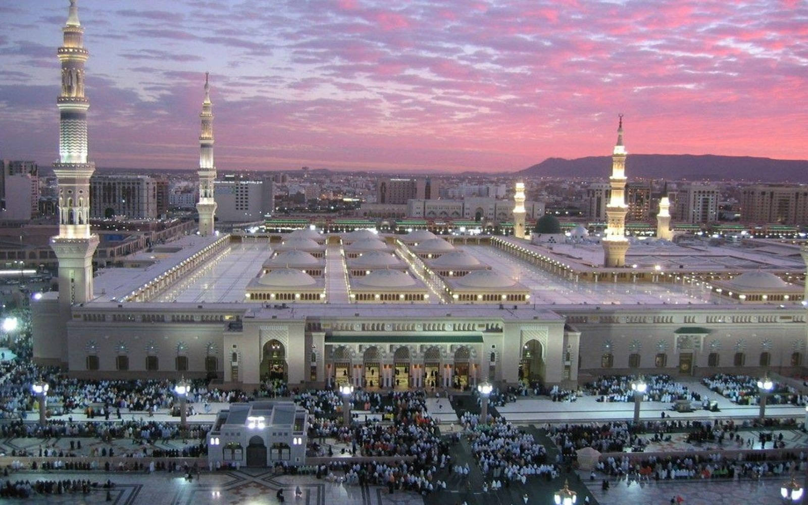 Makkah 桌布 壁紙 — 黃昏時分，粉紅色天空下，大清真寺燈火通明，庭院裡聚集了人群。