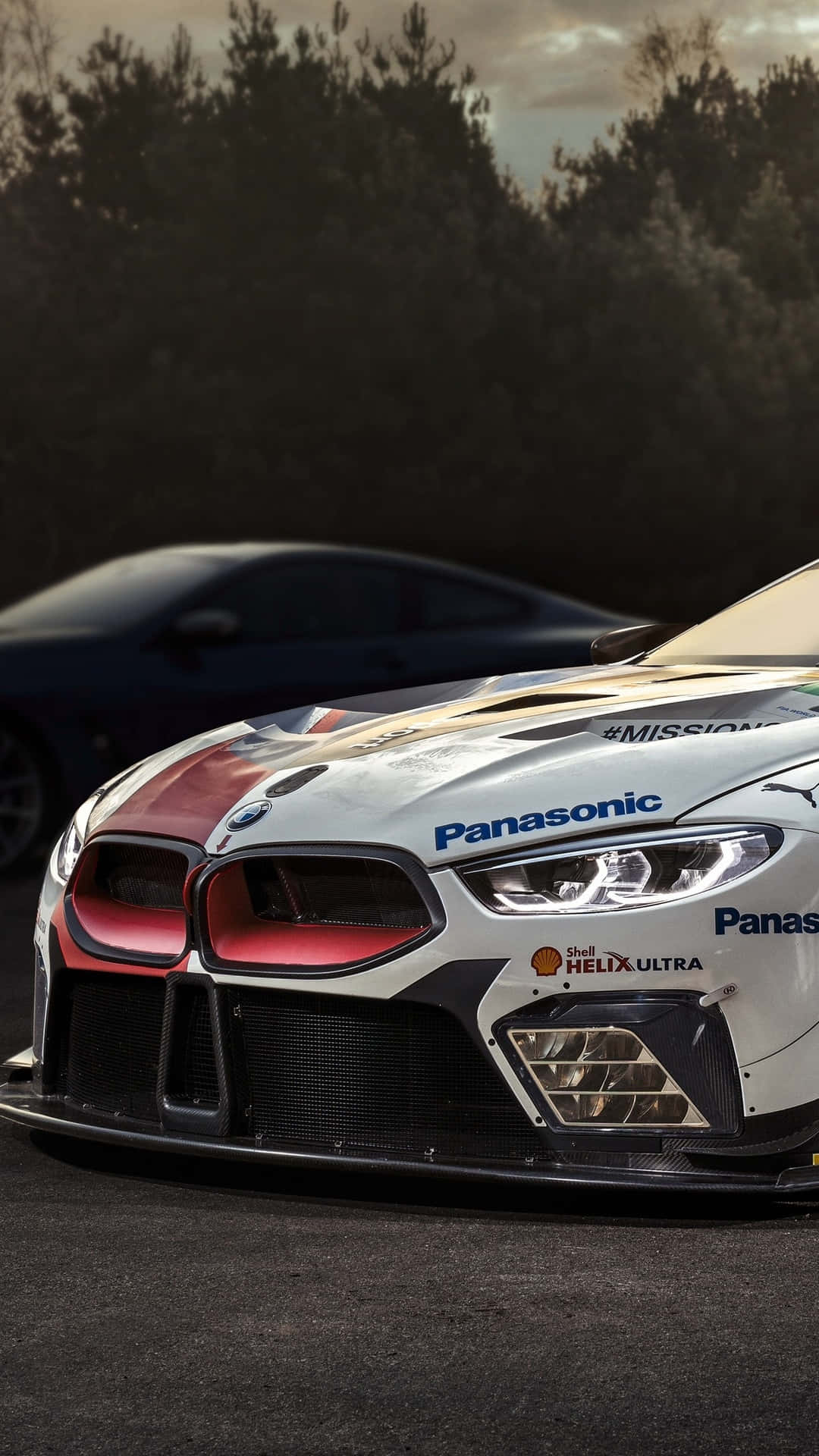 Bmw M8 4K 桌布 壁紙 — 黃昏時分，賽道上白色和紅色寶馬賽車的特寫，背景有樹木，車身有Panasonic和Shell標誌。
