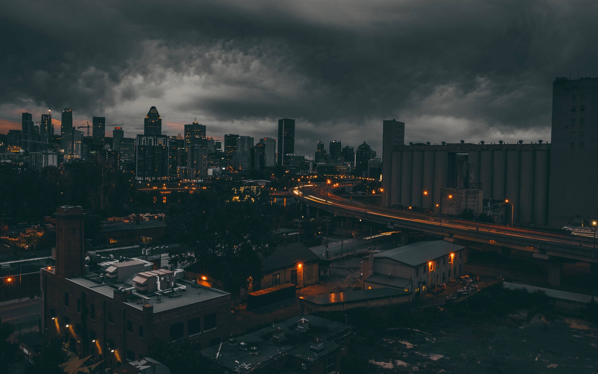黑暗的暴風雲籠罩著城市景觀，閃爍的路燈和黃昏時分飛馳的車頭燈。 — 黑暗城市 壁紙