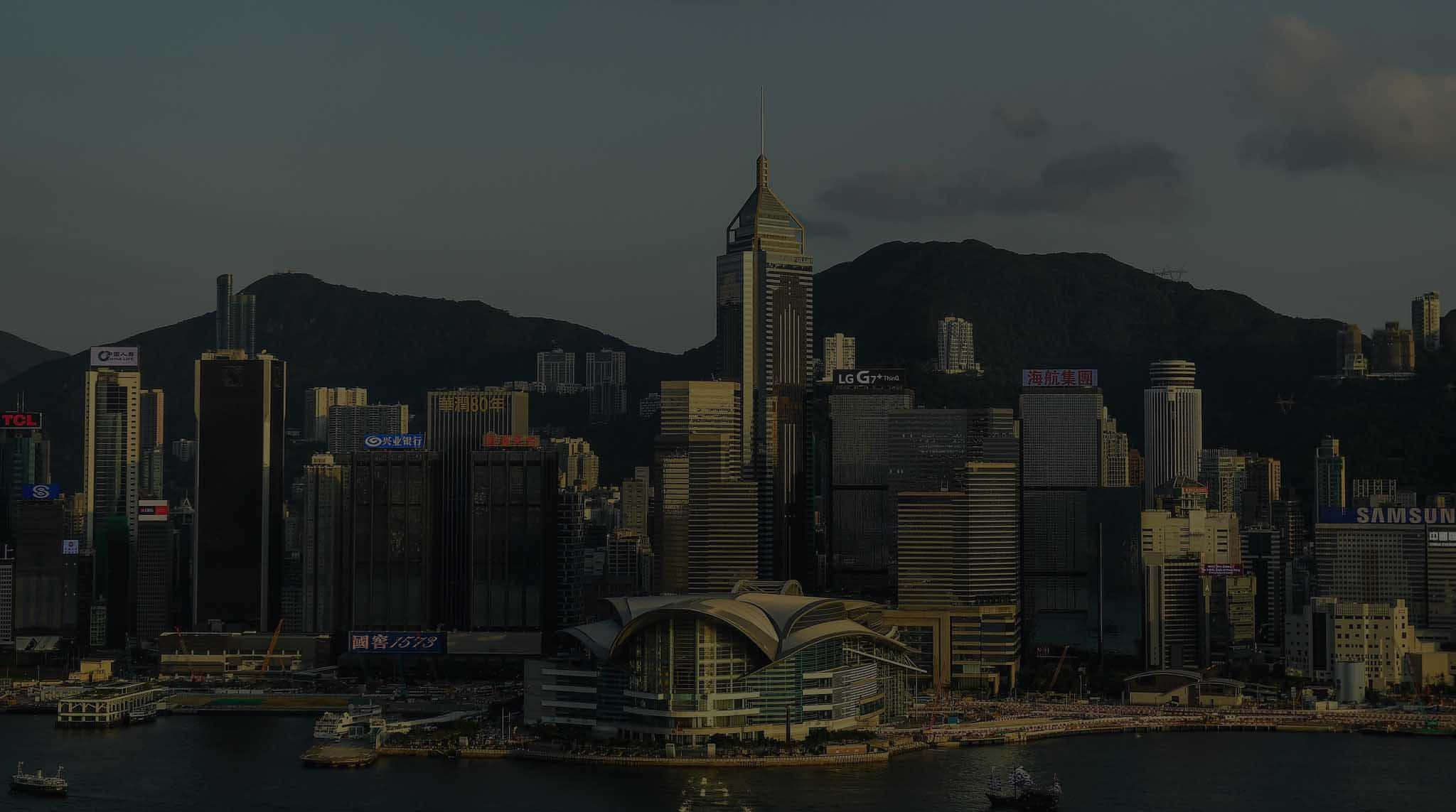 香港 桌布 壁紙 — 黃昏時分，香港天際線燈光昏暗，高聳的摩天大樓和山脈作為背景。