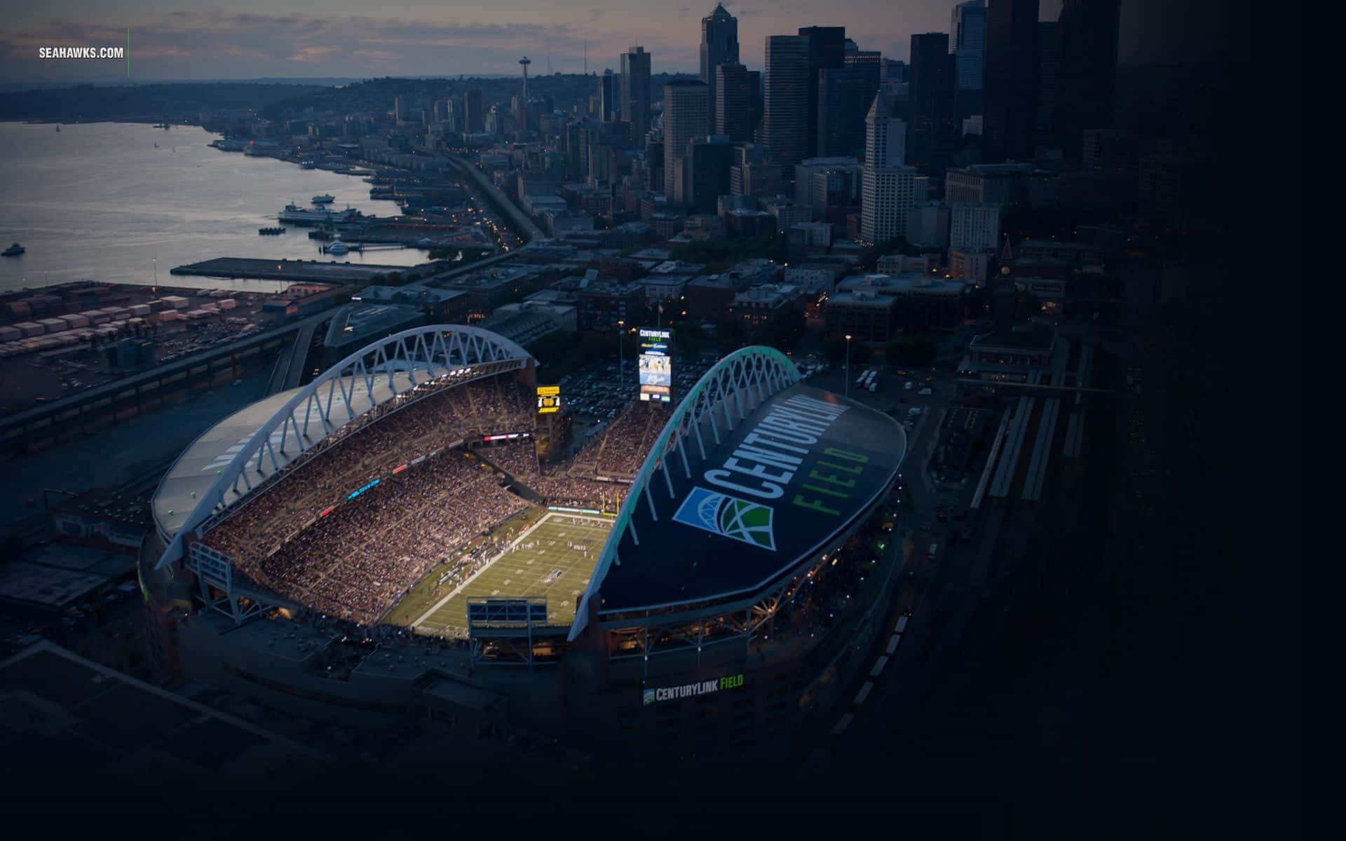 海鷹隊 桌布 壁紙 — 黃昏時分CenturyLink Field的鳥瞰圖，體育場燈光閃爍，背景是西雅圖天際線。