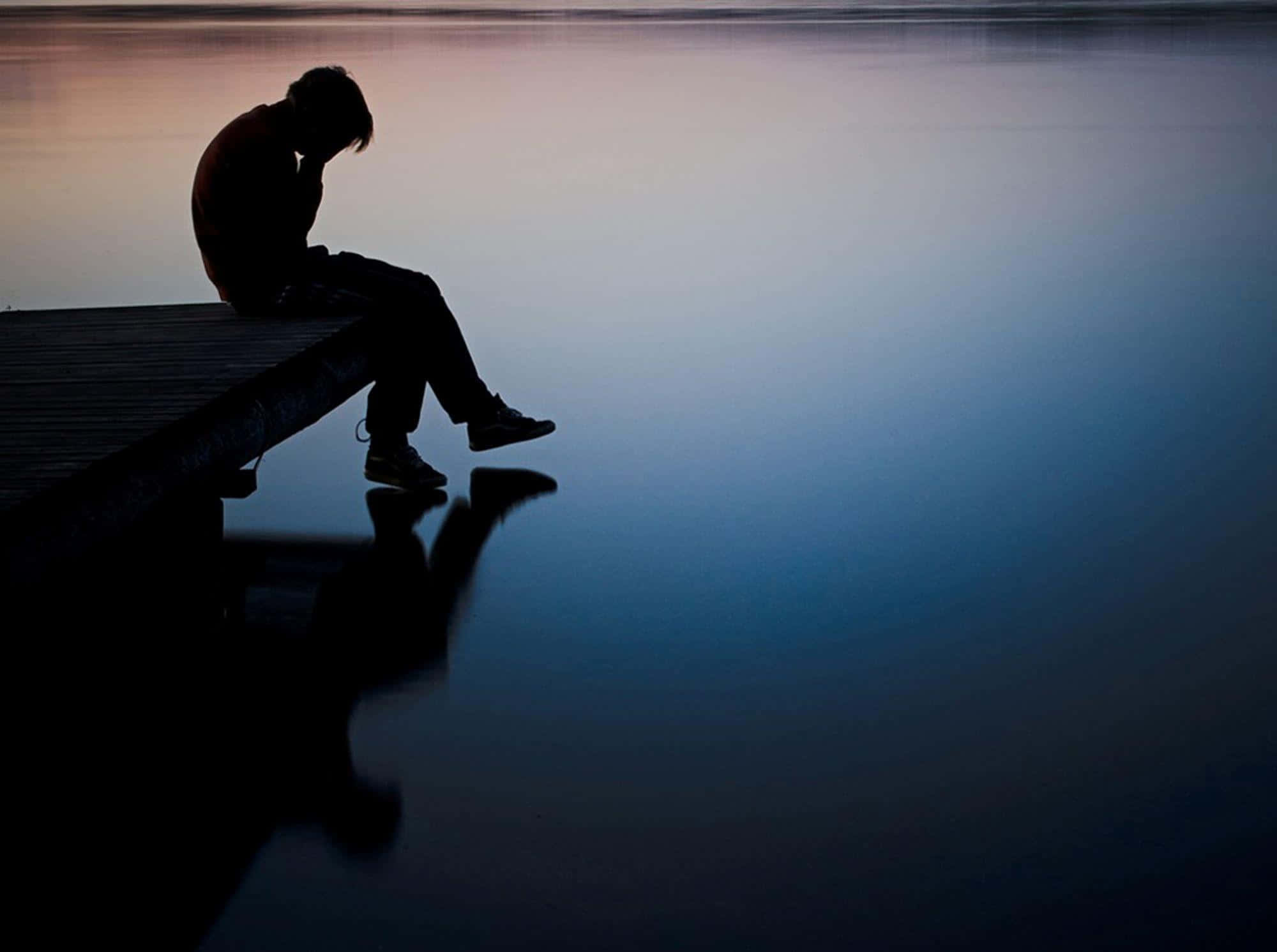 Depressing 桌布 壁紙 — 黃昏時分一個人獨自坐在碼頭上的剪影，平靜的水面倒映著他們的身影。