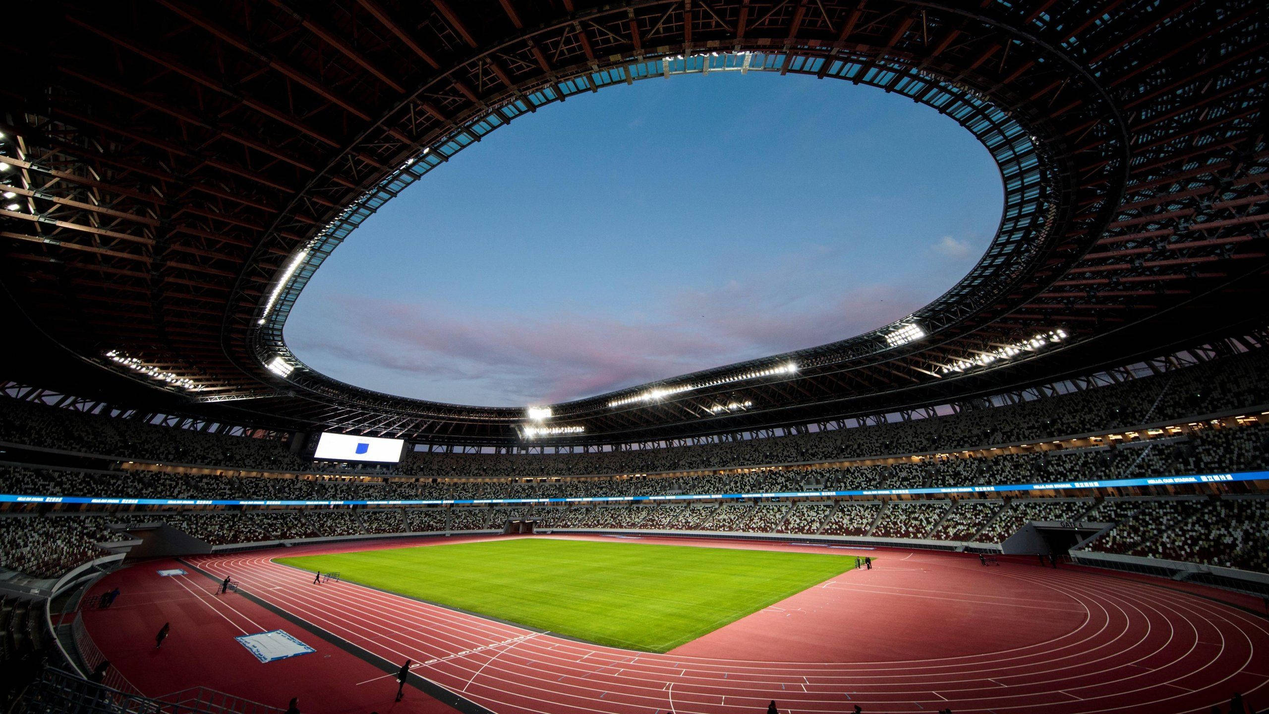 Stadium 桌布 壁紙 — 黃昏時分一個廣闊的現代化體育場，在暮色天空下擁有充滿活力的綠色場地和紅色跑道。