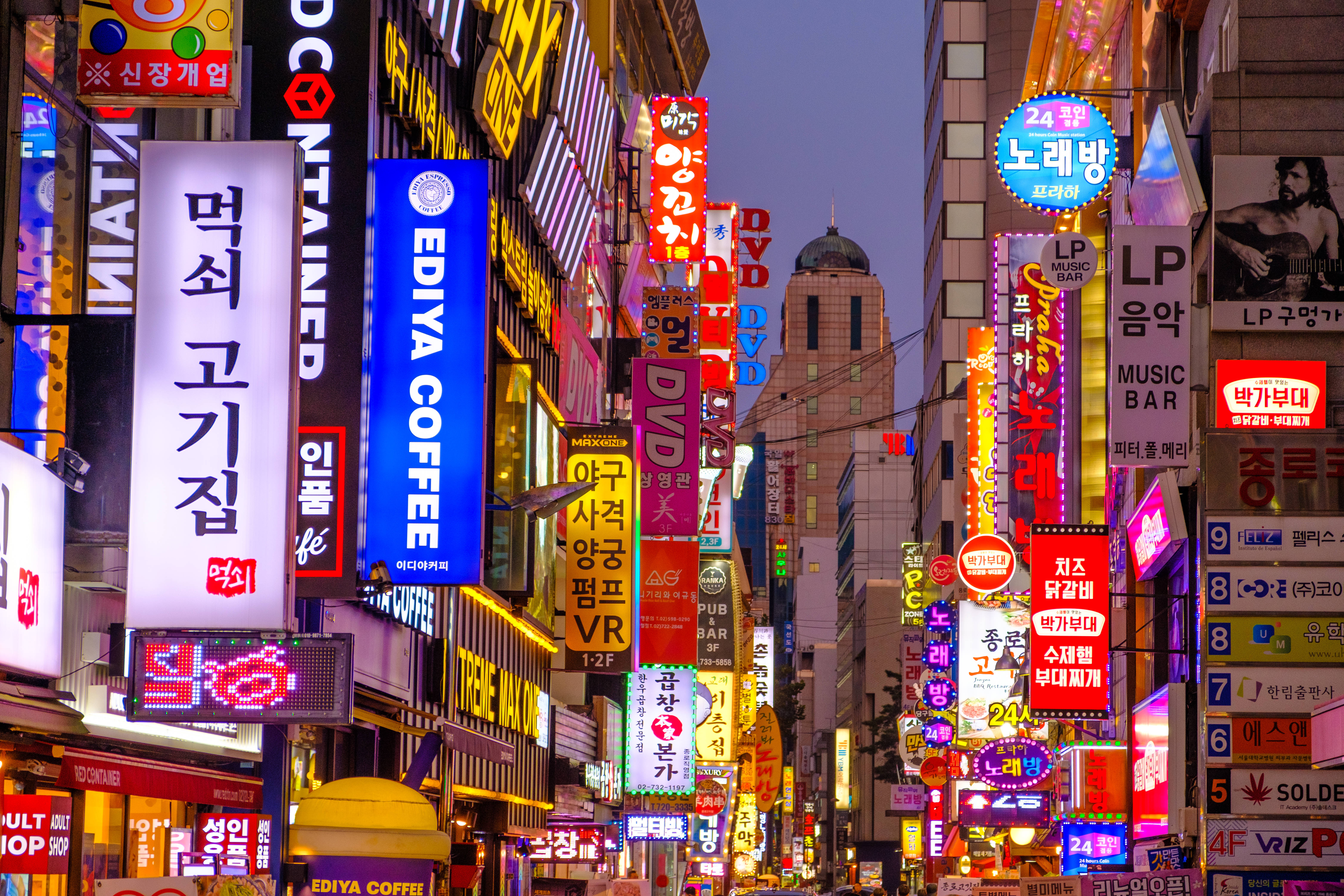 首爾 桌布 壁紙 — 黃昏時分一條令人眼花撩亂的城市小巷，充滿了發光的韓文霓虹招牌，宣傳咖啡館、酒吧和商店。
