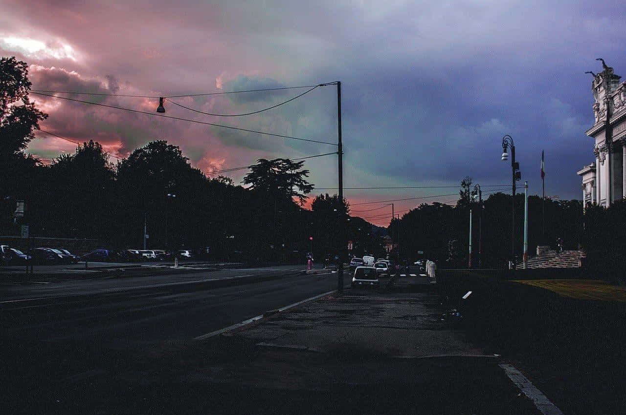 Aesthetic Grunge Laptop 桌布 壁紙 — 黃昏時分一條充滿氣氛的城市街道，戲劇性的粉紅色和紫色雲彩籠罩著剪影般的樹木和建築物。