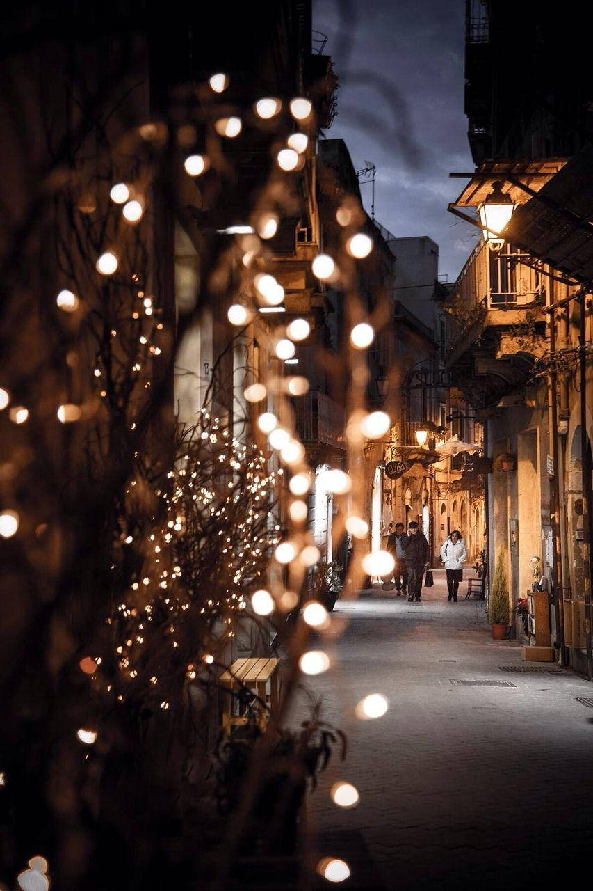 Christmas Lights Aesthetic 桌布 壁紙 — 黃昏時分一條狹窄的鵝卵石小巷，溫暖的串燈和柔和燈籠在濕石上投下金色倒影。